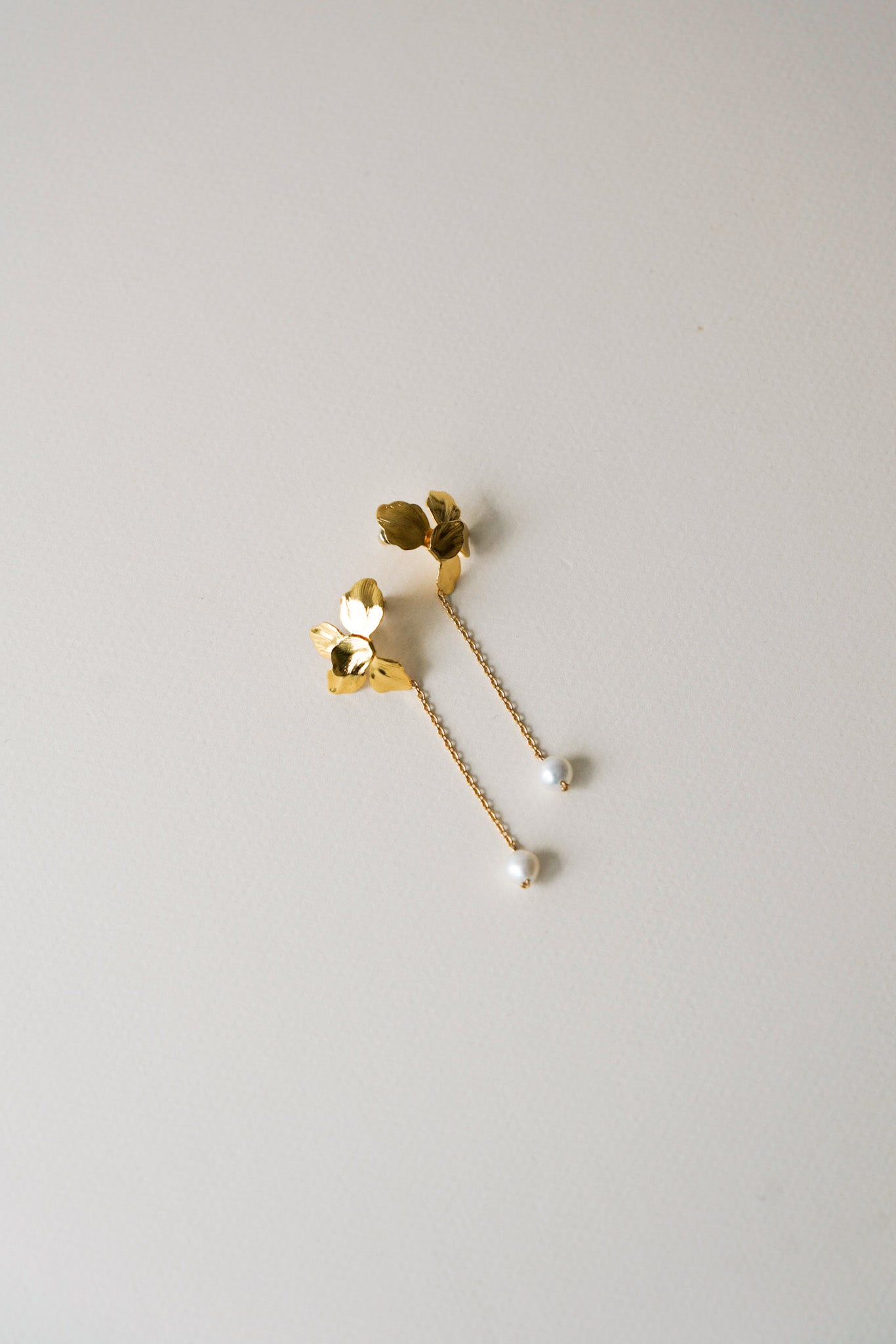 Boucles d’oreilles longues et élégantes, composées d’une fleur dorée en partie haute, délicatement reliée par une fine chaîne à une perle de culture suspendue en bout. Une création aérienne et poétique, parfaite pour une mariée ou une tenue raffinée.