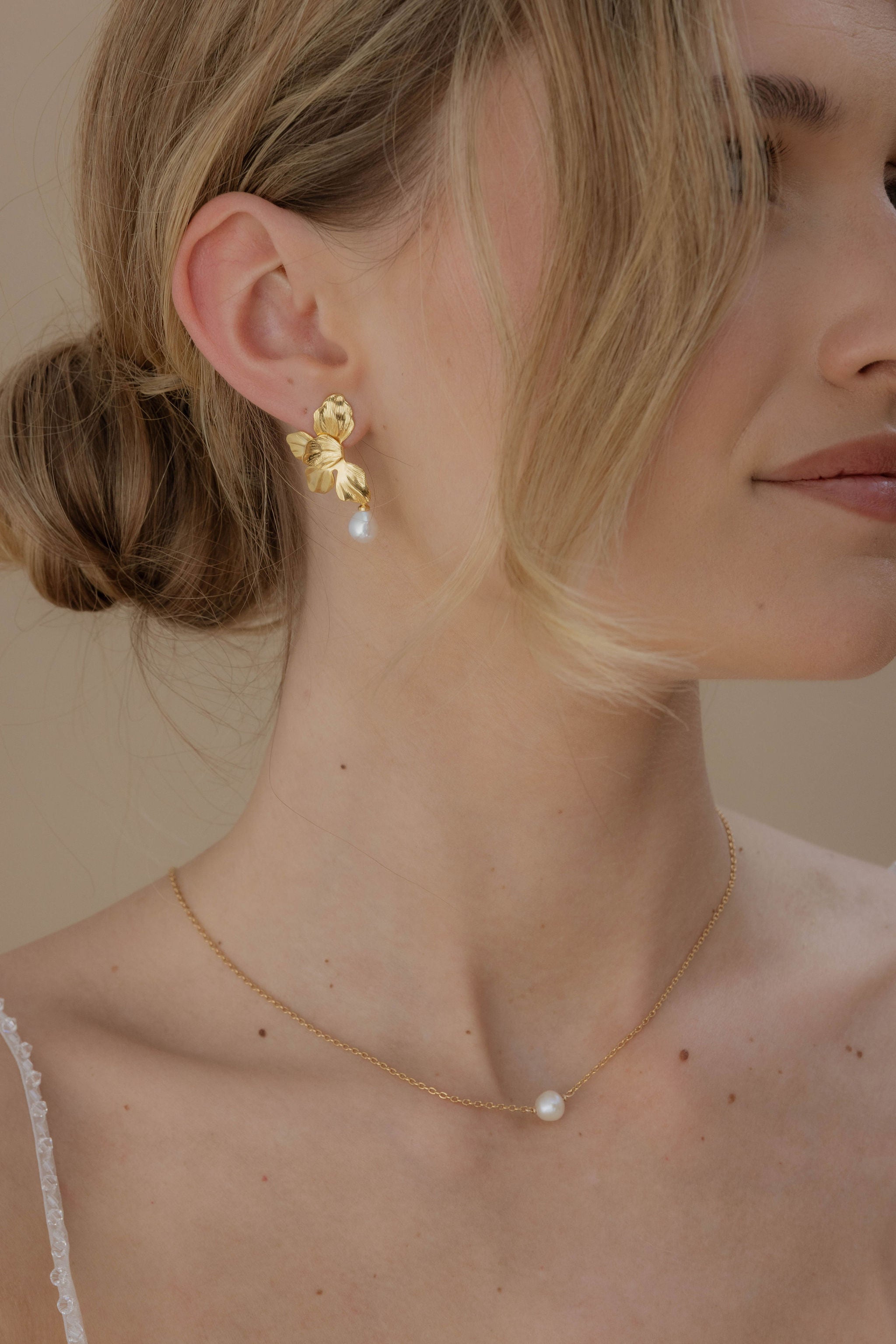 Portrait de femme qui regarde vers le cote, elle porte des boucles d'oreilles Roma florales ornées de perles et un collier court avec un perle ronde au milieu.