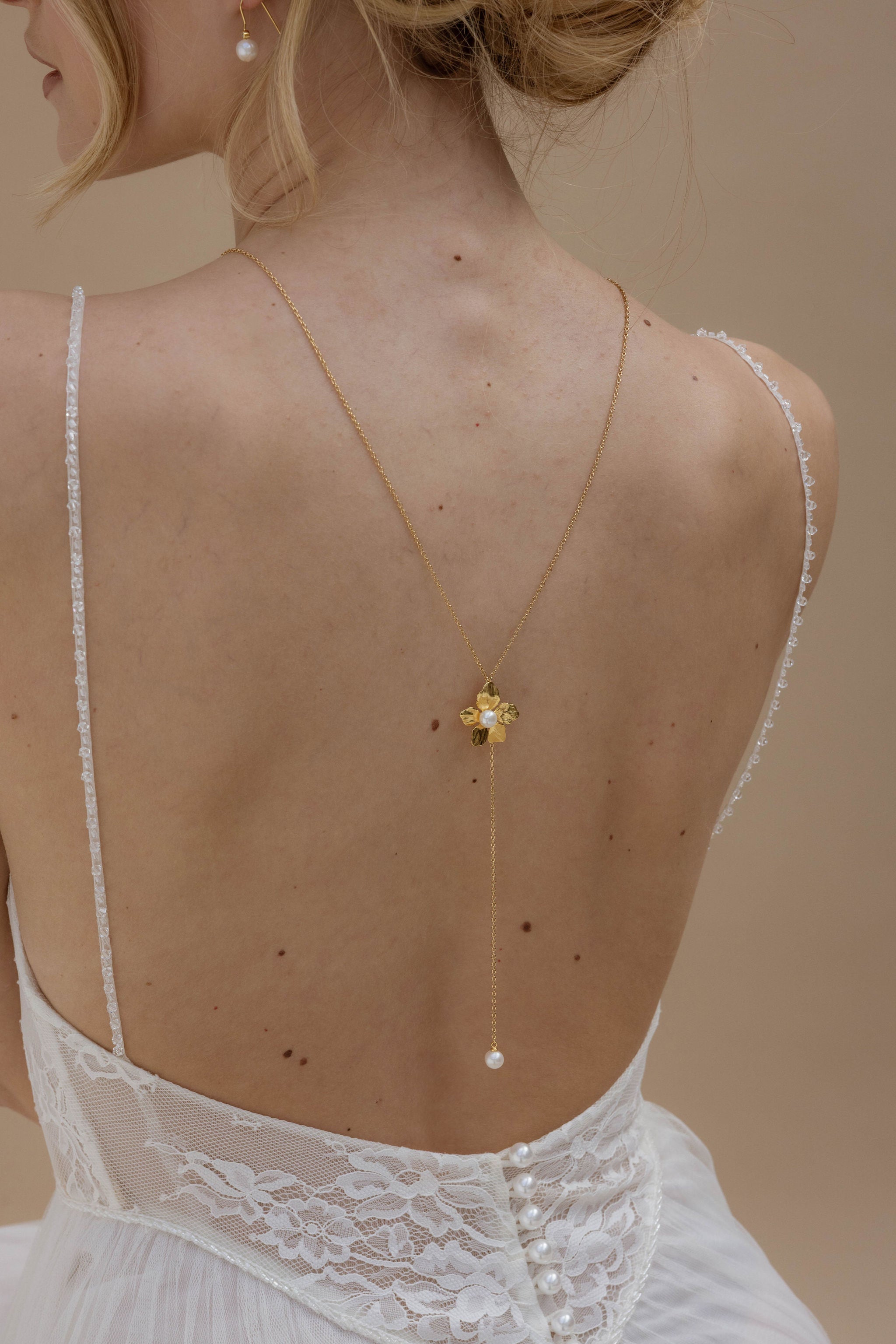 Femme en robe de mariee avec un un dos nu qui porte un collier de dos avec une fleur au milieu et des perles de culture.