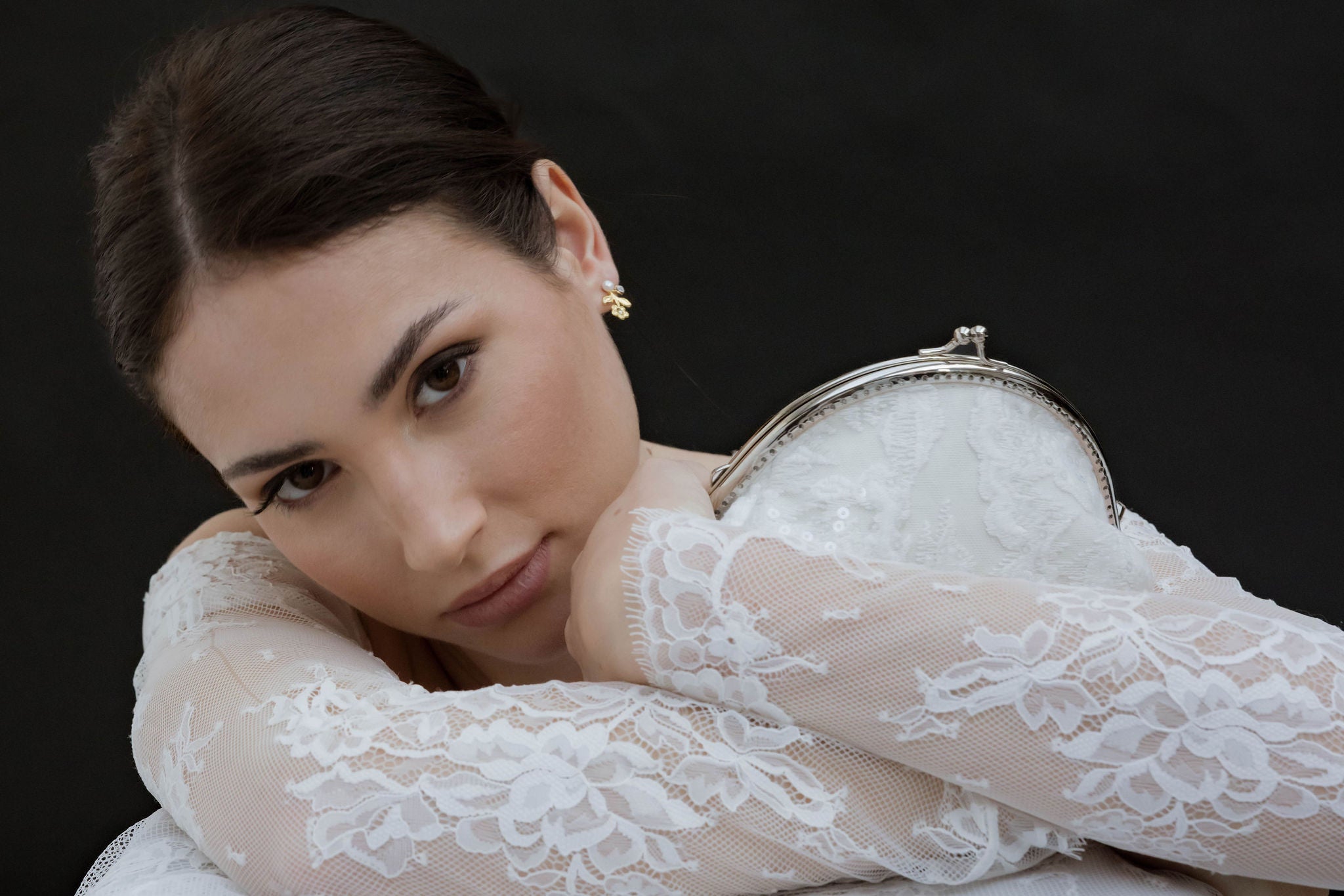 Mariée avec robe de mariée en dentelle, des boucles d'oreilles florales et porte un sac en dentelle et sequins aux motifs floraux