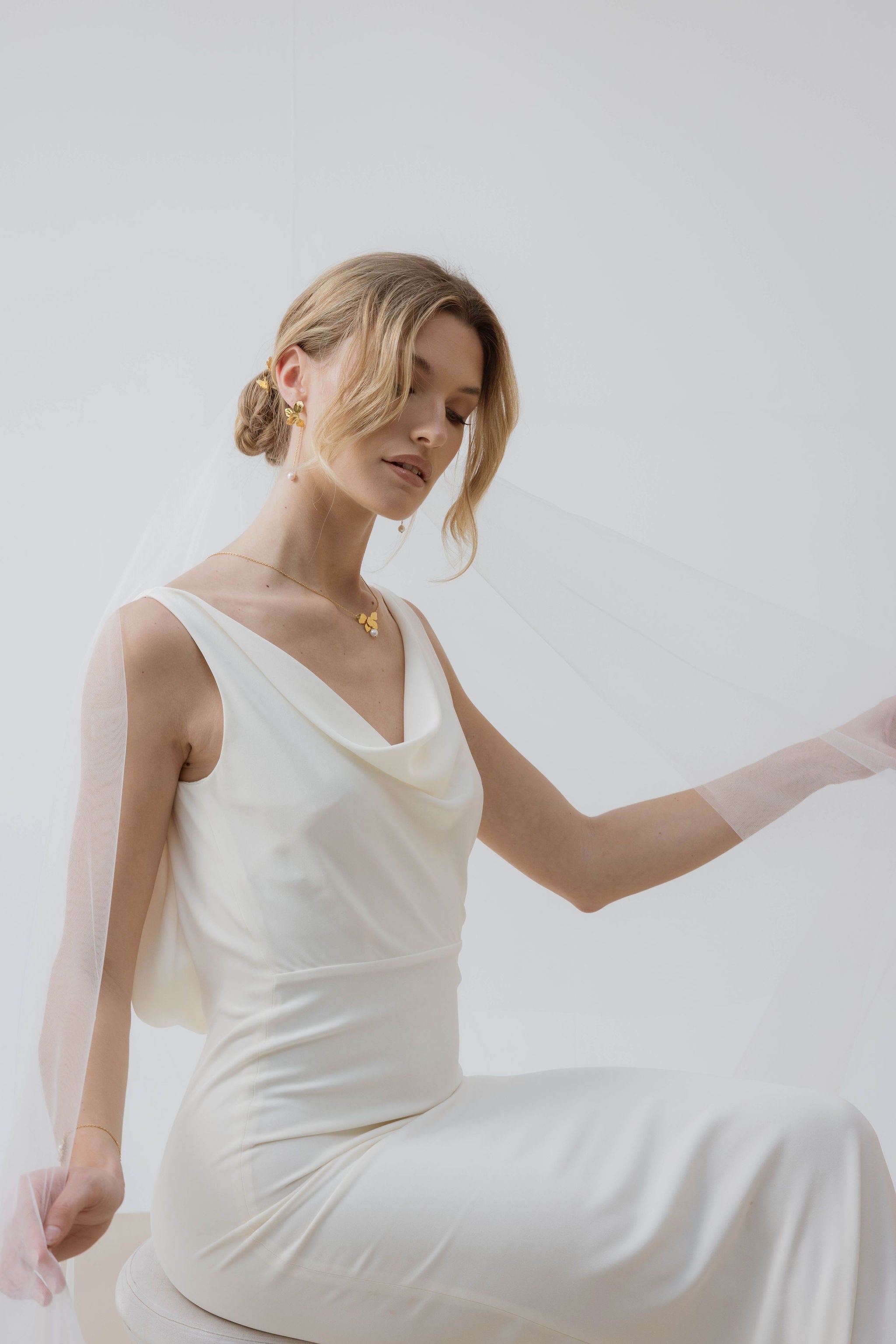 Mariée portant des boucles d'oreilles pendantes avec des perles aux bouts, vêtue d'une jolie robe blanche et coiffée d'un chignon élégant, pour un look raffiné et romantique