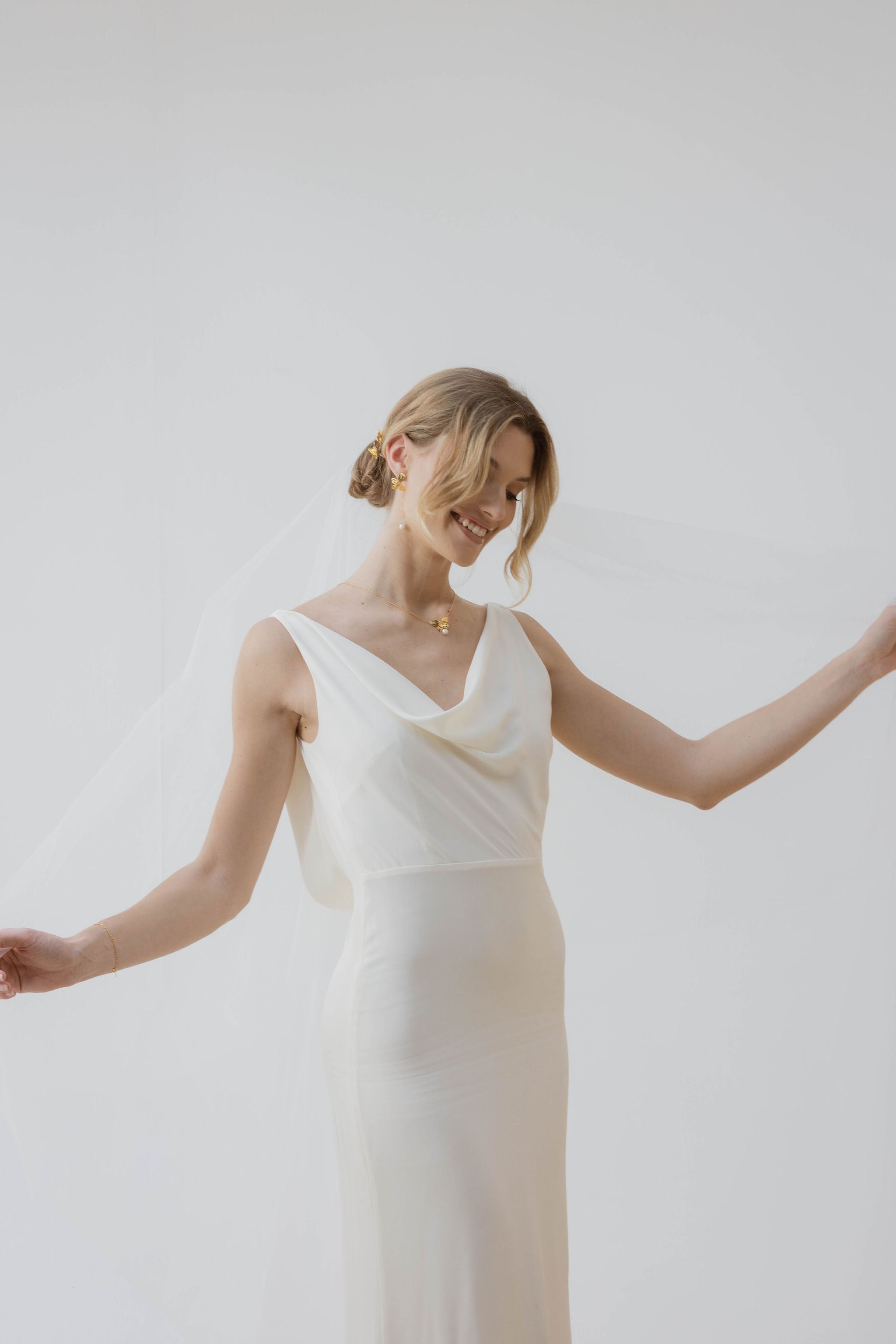 Mariée portant des boucles d'oreilles pendantes avec des perles aux bouts, une jolie robe blanche, un chignon élégant et un voile délicat, pour un look romantique et raffiné