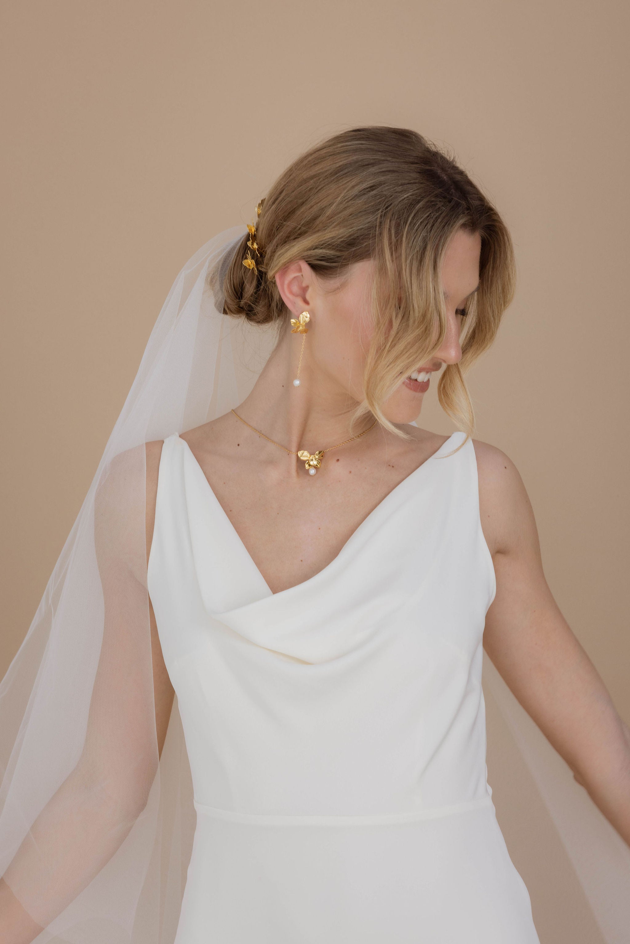 Mariée avec des boucles d'oreilles pendantes ornées de perles aux bouts, une jolie robe blanche, un voile et un chignon sophistiqué, créant un look élégant et intempore