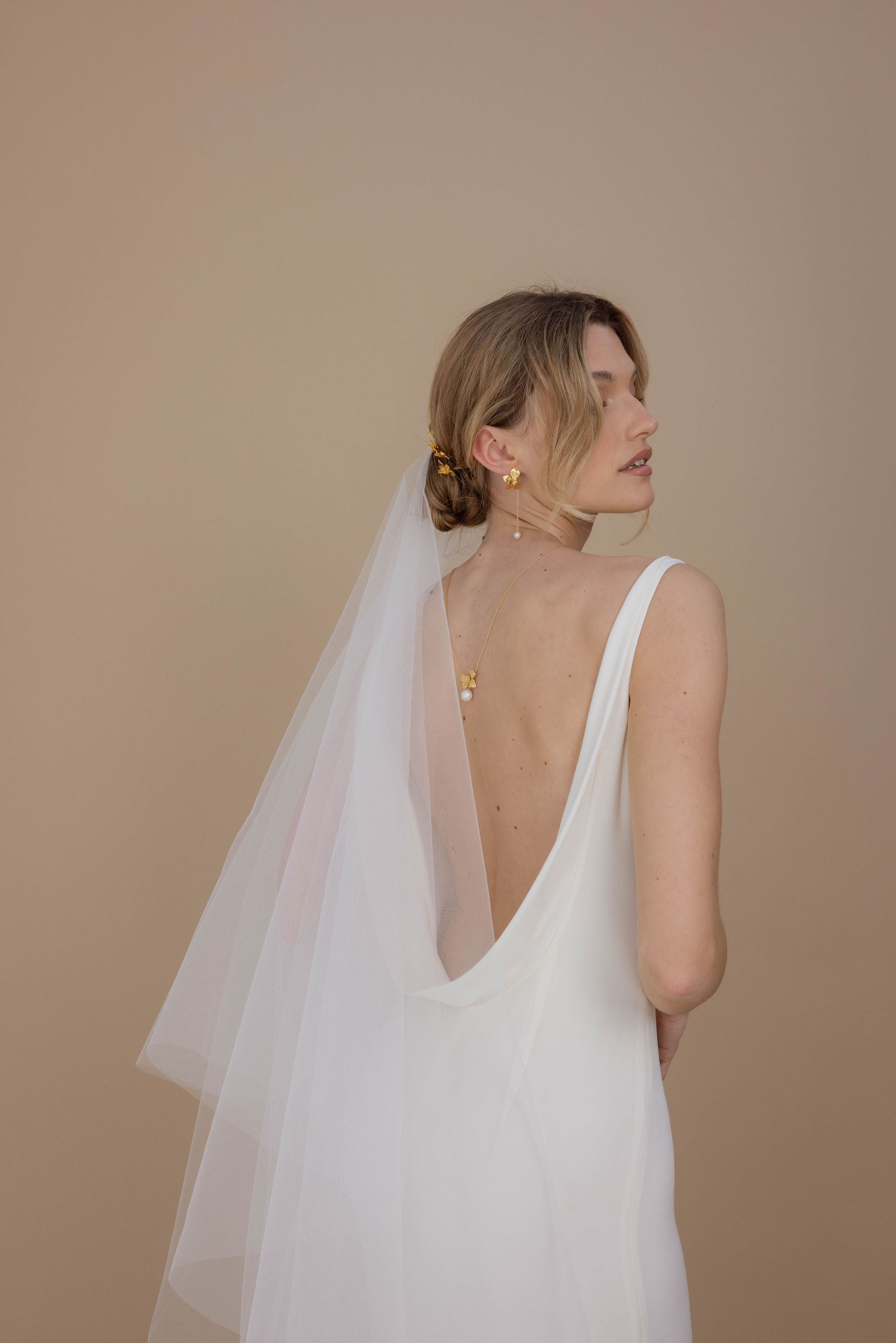 Chignon de mariée orné de pics floraux et voile, accompagné d’un collier de dos élégant et de boucles d’oreilles en perles et floral.