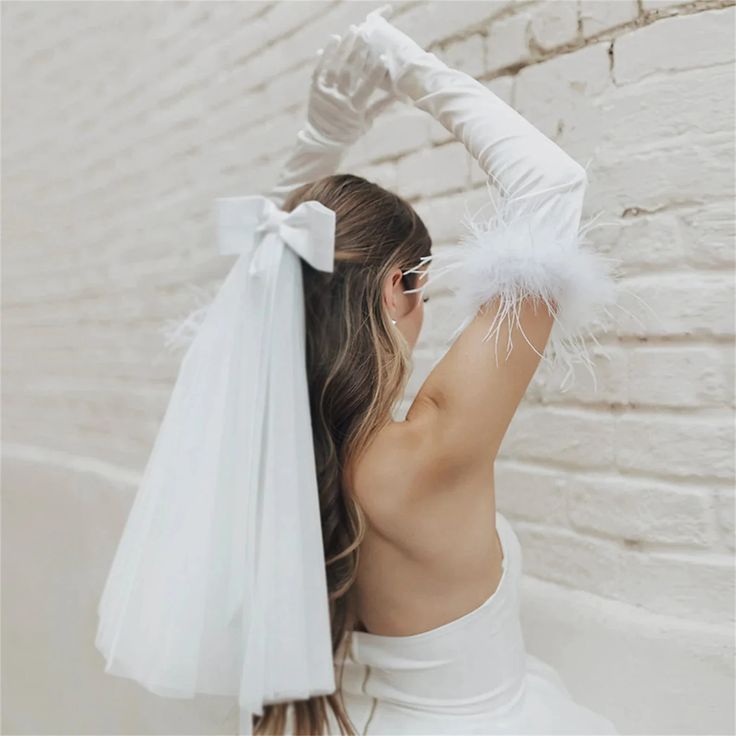 Femme portant une tenue de mariée avec beaucoup d'accessoires de mariage comme des gants satinés avec des plumes ainsi qu'un noeud aux cheveux