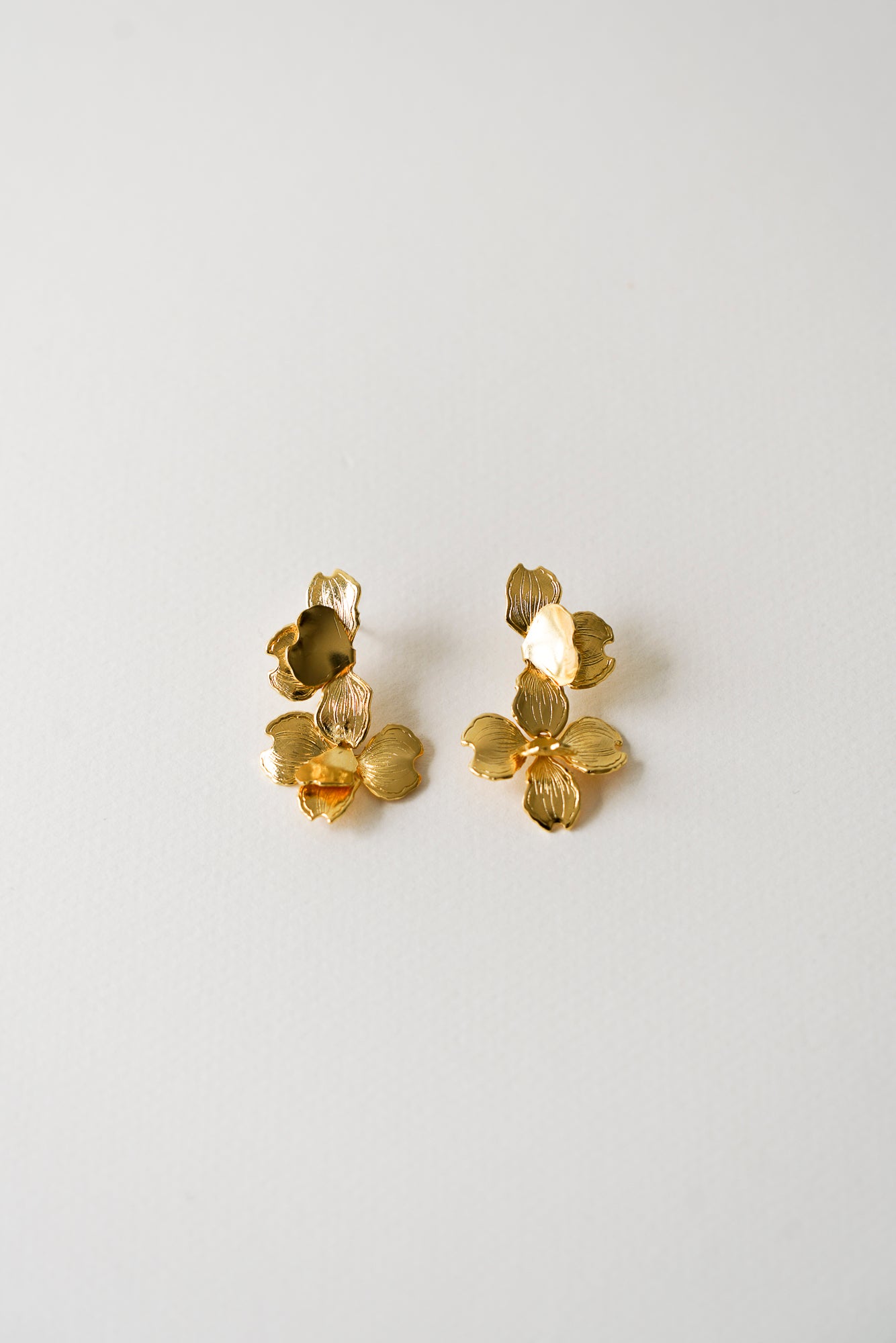 Boucles d'oreilles fleur de mariage en version dorée posées usr un fond uniforme beige clair