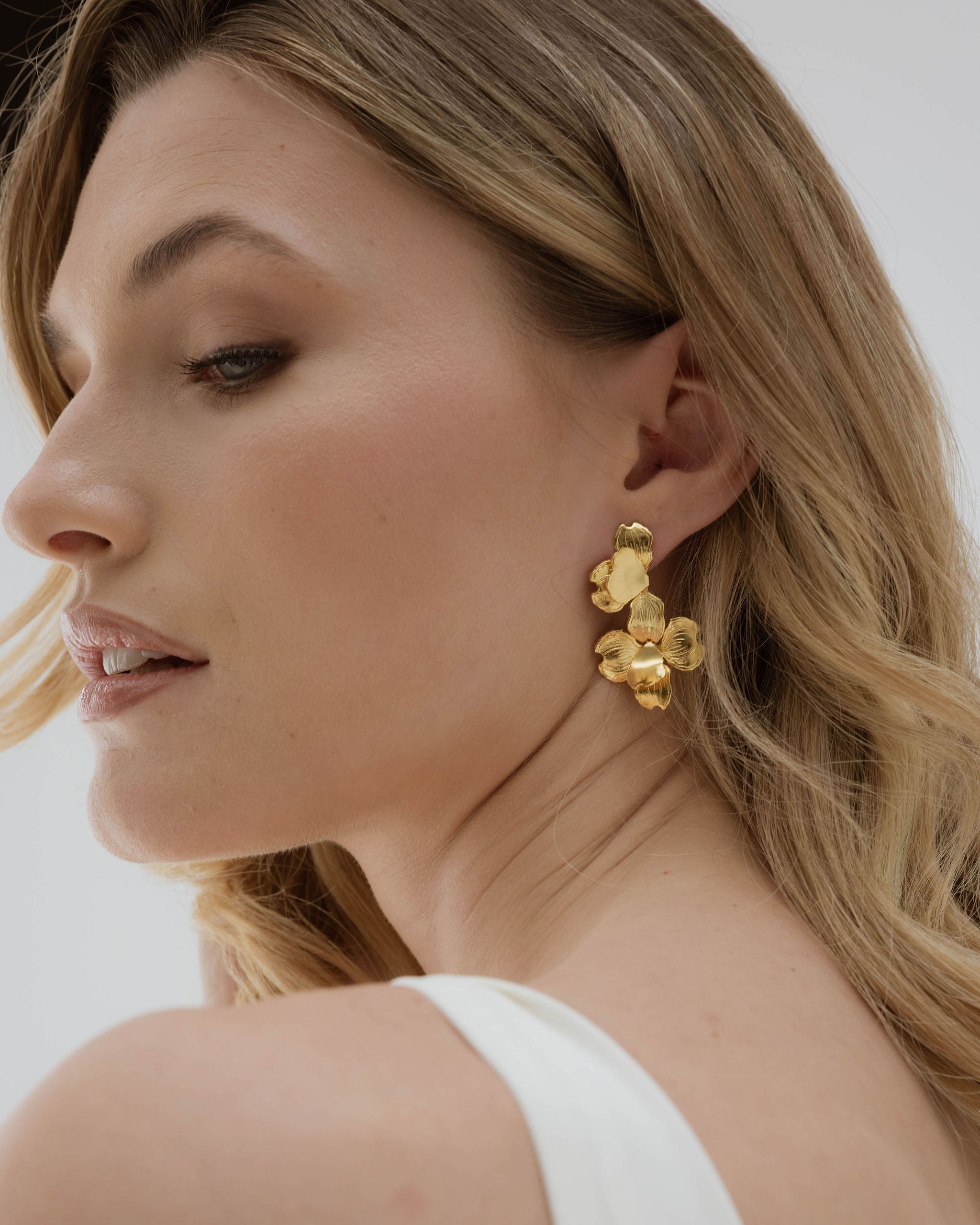 Mariée portant une robe blanche simple, coiffée d’un chignon bas, sublimée par un bijou clip floral doré à l’oreille pour une touche élégante et naturelle.