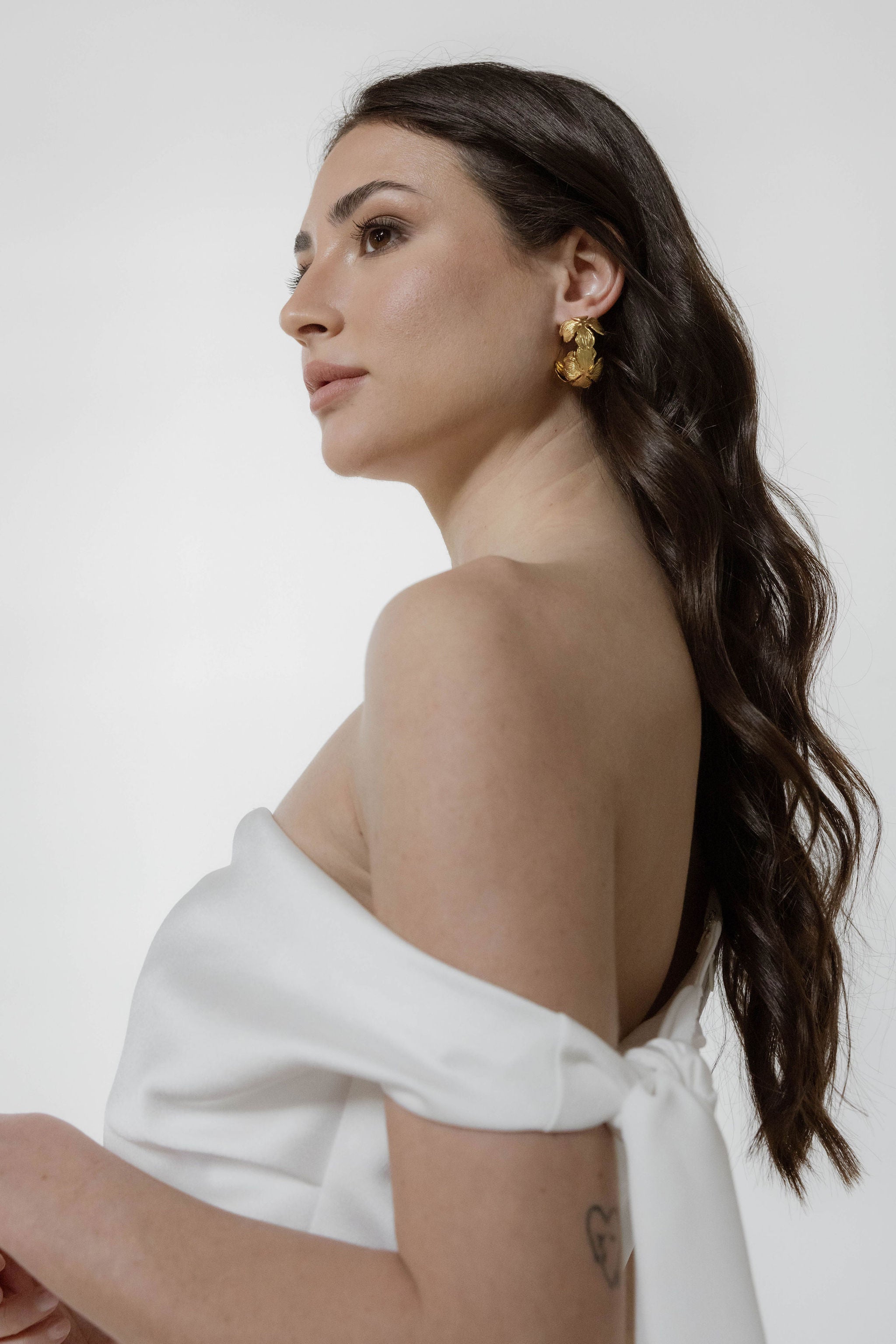 Mariée en robe bustier, les cheveux ondulés et détachés, mise en valeur par de grandes créoles florales qui encadrent délicatement son visage.