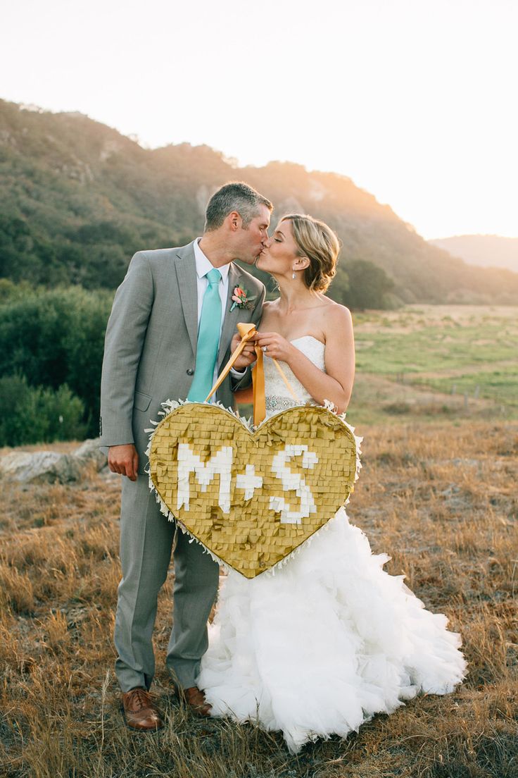 Un couple de mariés avec une piñata ornée de leurs initiales, illustrant des alternatives au lancé de bouquet et des idées originales pour des activités de mariage.