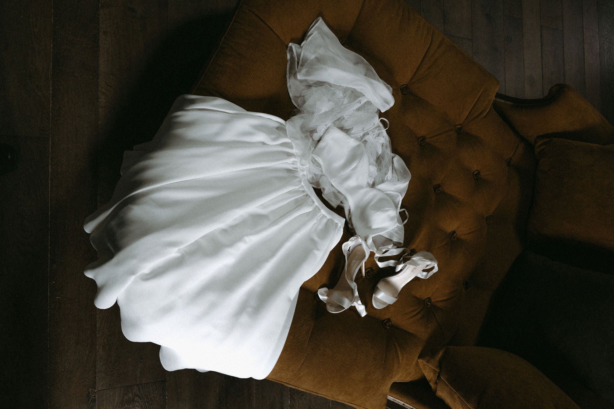 Photo esthétique de robe de mariée deux pièces élégante posée sur un canapé, à côté des chaussures de mariée à talons blanches élégantes, photo contrastée, inspiration élégante de tenue de mariée pour un mariage en château