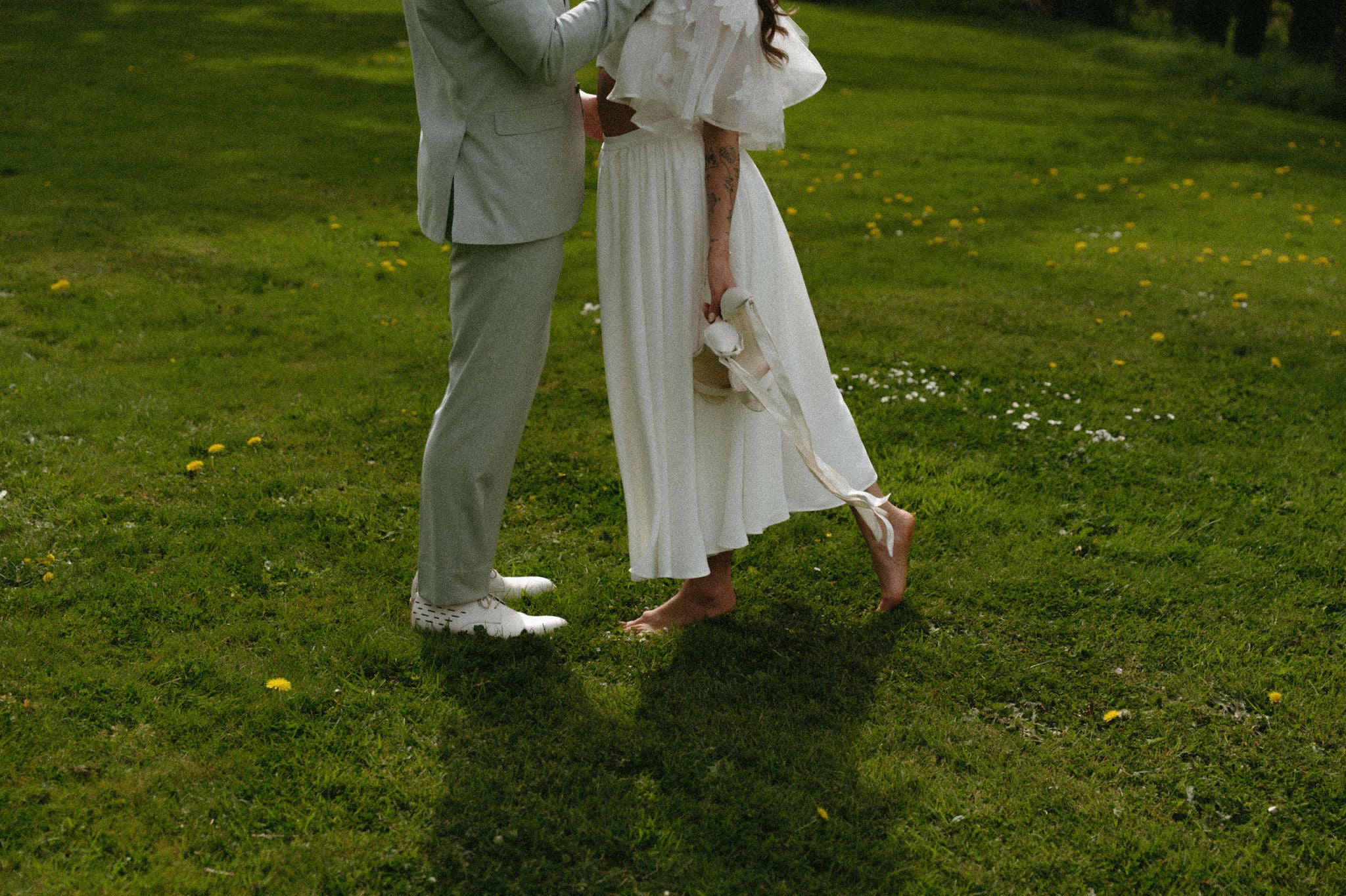 Photo de couple qui s'embrasse, mariée pieds nus dans l'herbe, couple romantique, mariage élégant; la mariée tient ses talons dans sa main, jardin de château fleuri, mariage au château, inspiration mariage élégant, blog mariage, domaine du mezo