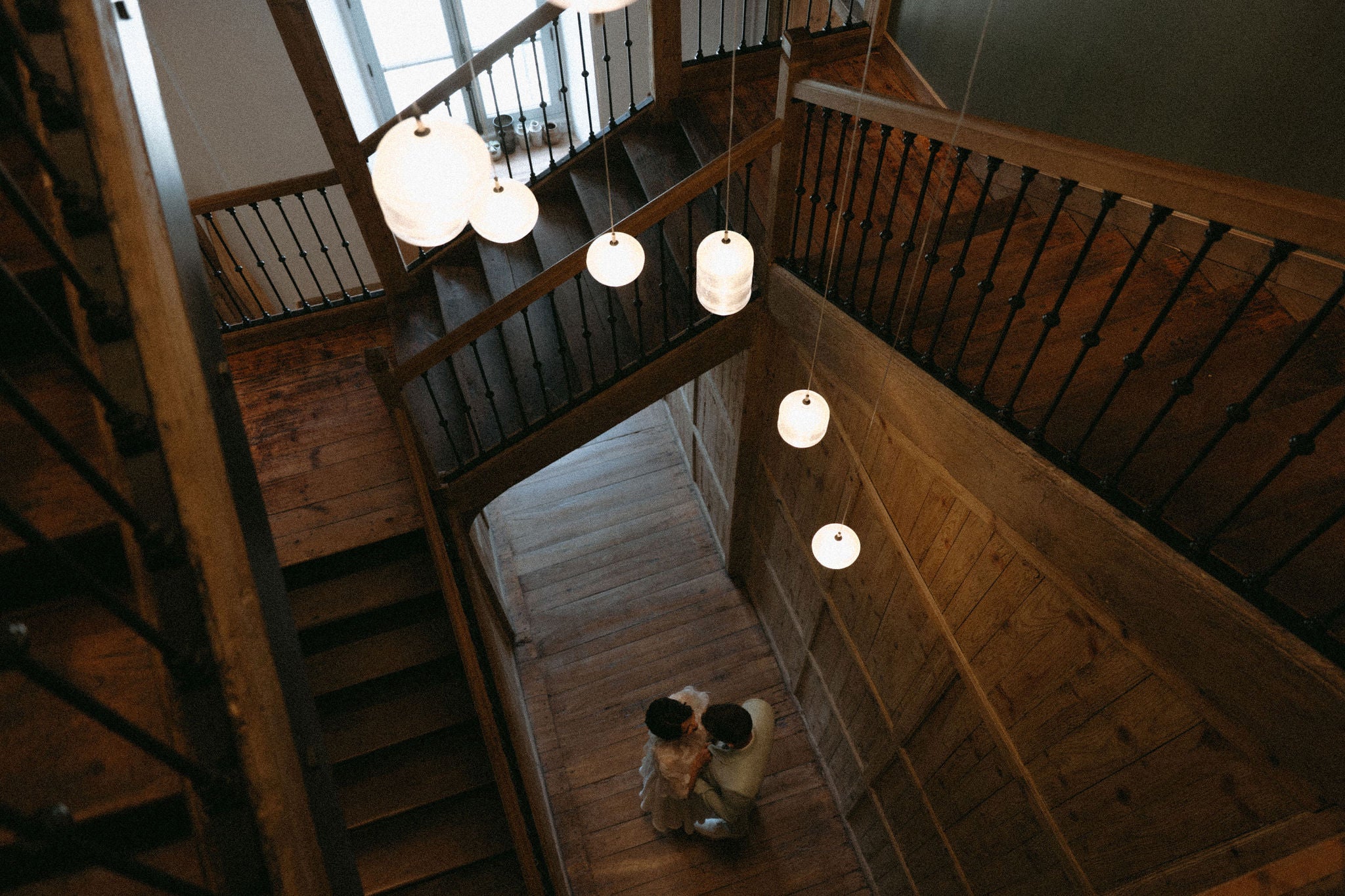 Photo romantique de couple dans une cage d'escalier en bois au château, couple marié, mariée en robe deux pièces et mari en costume vert d'eau clair, couple amoureux qui s'embrasse, réception de mariage élégante au château