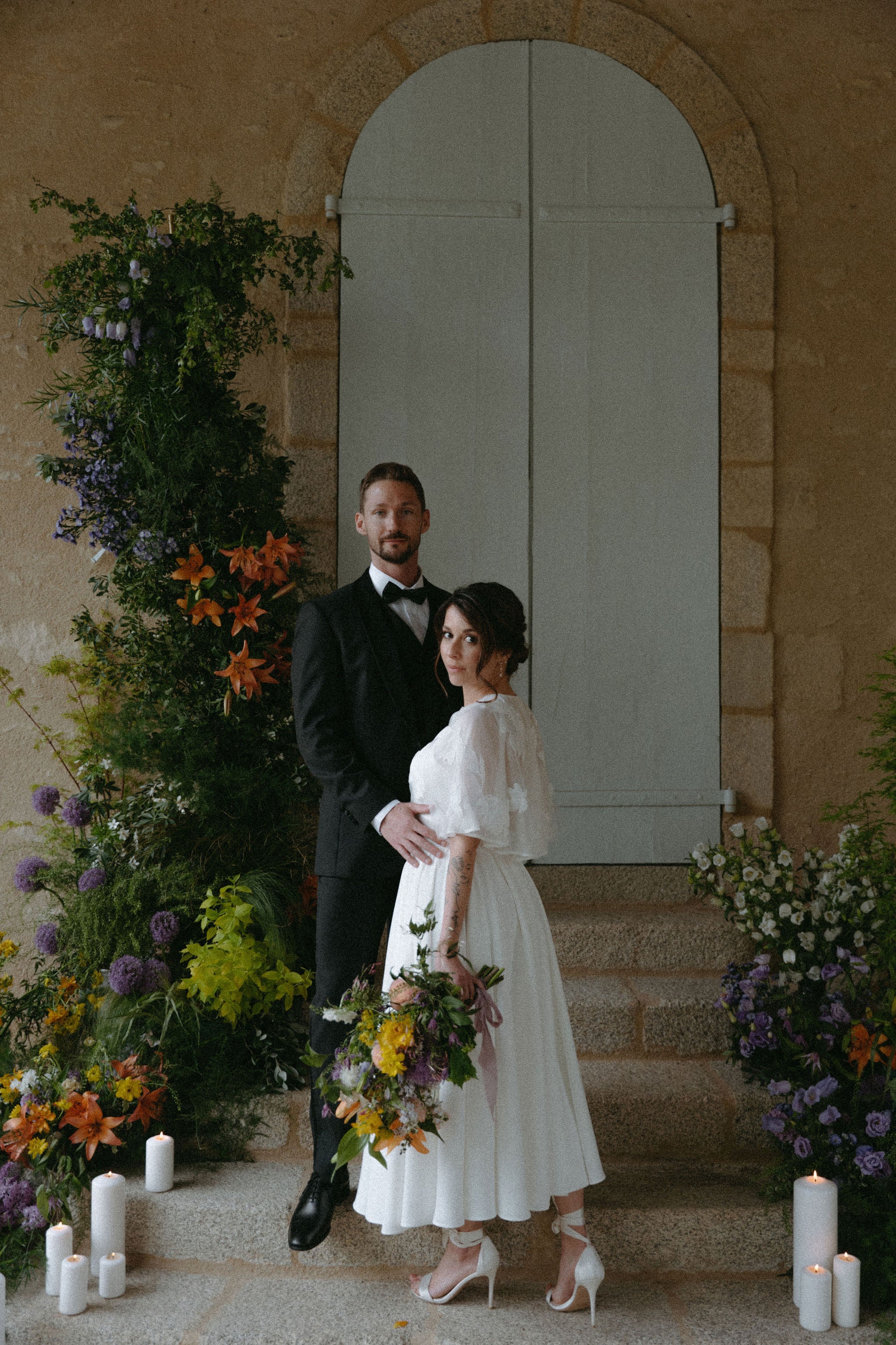 Photo verticale d'un couple marié qui pose, le mari tient la femme, femme en robe de mariée qui tient un bouquet de fleurs, mariée élégante, chaussures à talons de mariée élégante, tenue de mariée, couple mariage romantique en château, mariage élégant en château, fleurs mariage