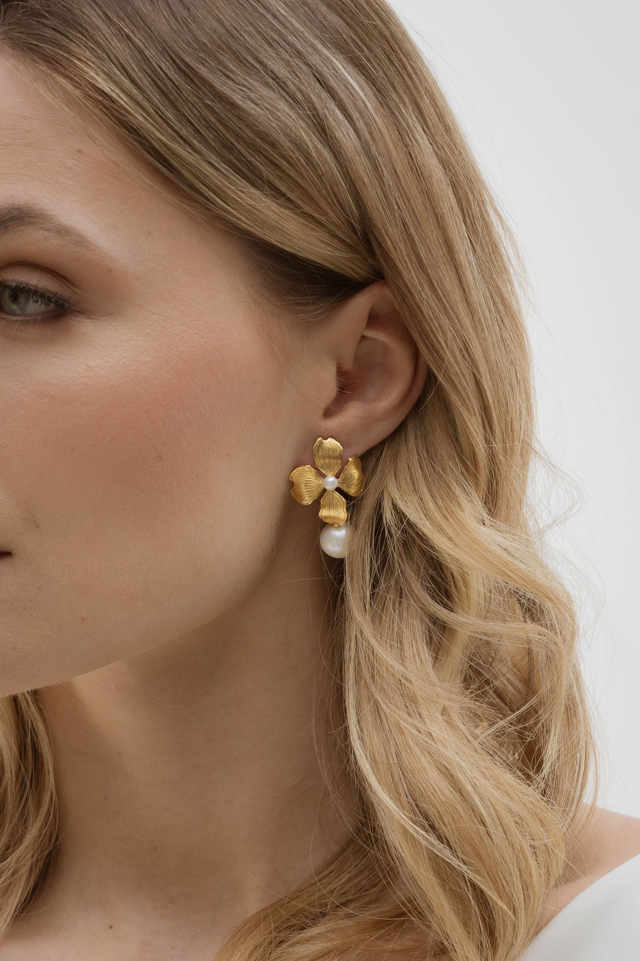 La mariée, vêtue d’une robe blanche simple et cheveux lâchés, sublime son look avec des boucles d’oreilles florales en perles, ajoutant une touche de raffinement délicat.