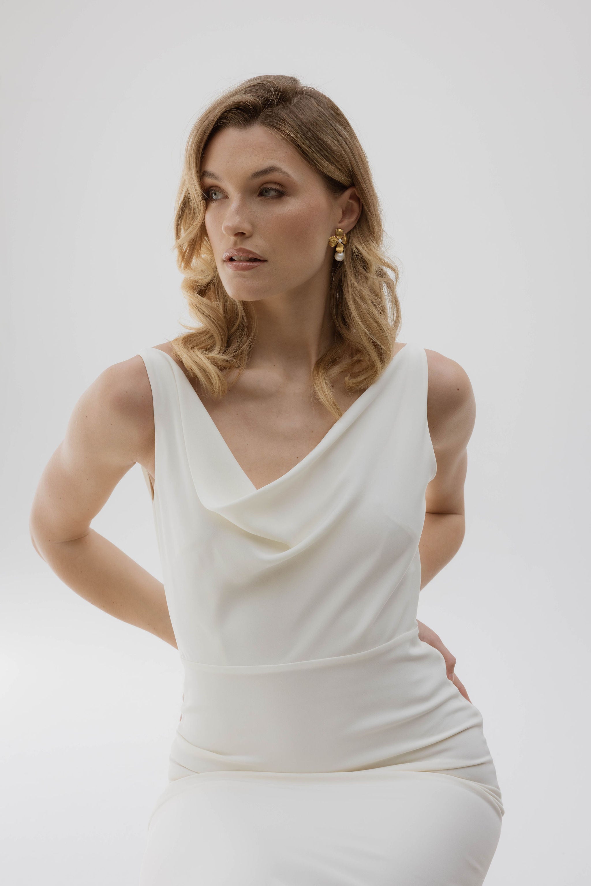 Mariée en robe blanche simple, cheveux lâchés, avec de magnifiques boucles d'oreilles florales en perles, pour un look naturel et élégant.