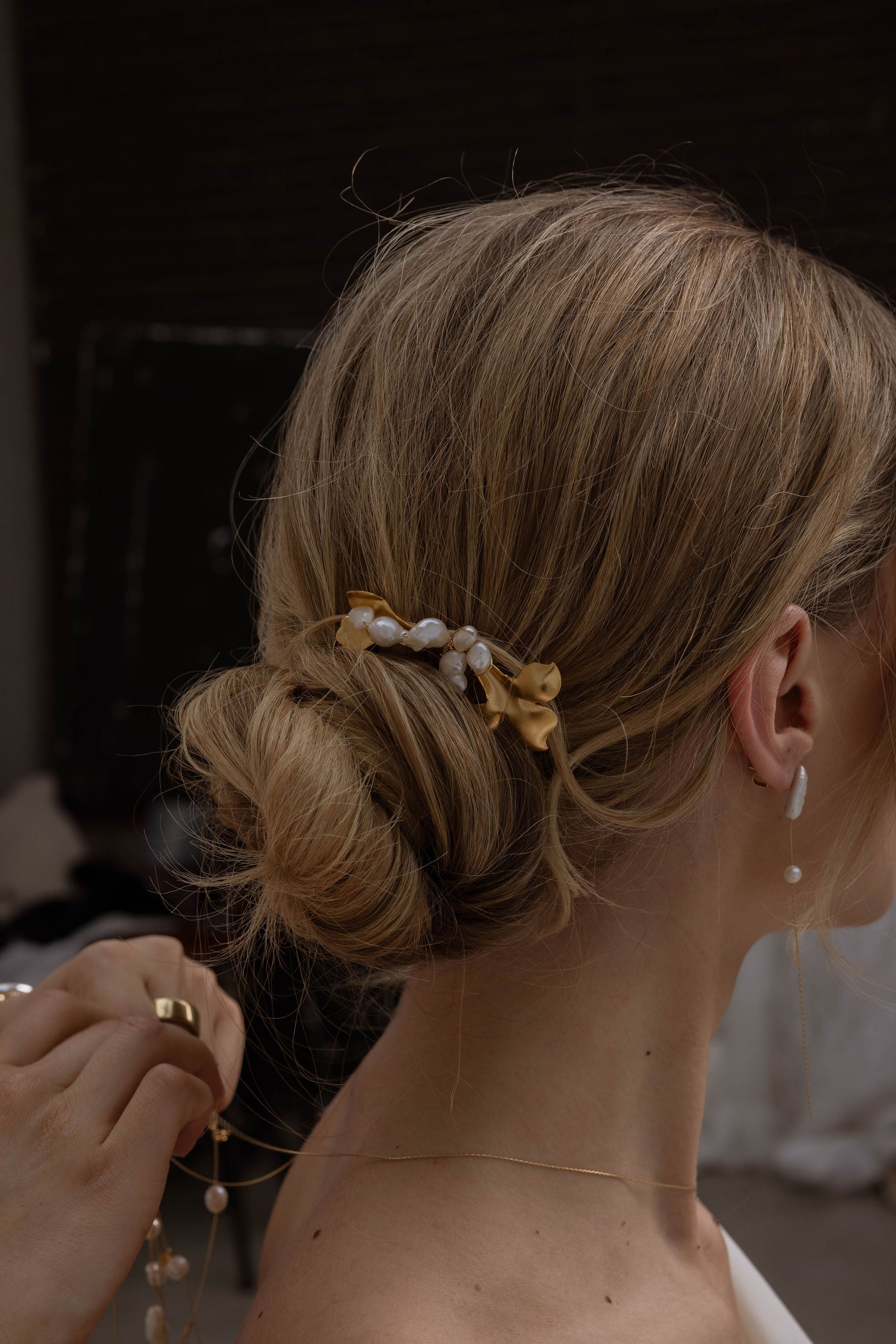 Mariée de profil avec un joli chignon bas, portant des boucles d’oreilles pendantes à deux perles.