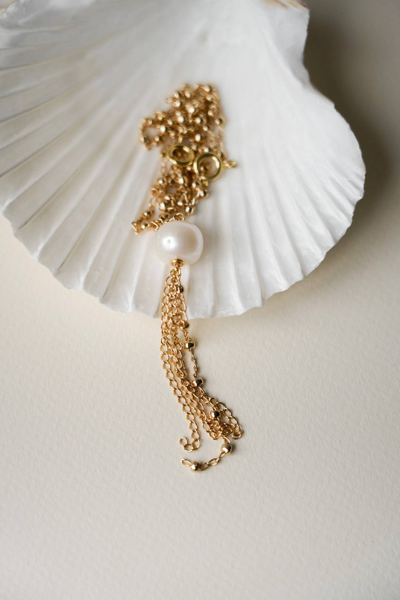 Collier porté dans le dos, composé d’une fine chaîne agrémentée de petites billes délicates qui ajoutent une touche d’élégance et de finesse. À l’extrémité du collier, une perle blanche est délicatement posée dans un coquillage nacré, mettant en valeur le détail raffiné du bijou. Ce design apporte un contraste subtil entre la brillance des perles et la texture naturelle du coquillage, créant un effet à la fois élégant et poétique.