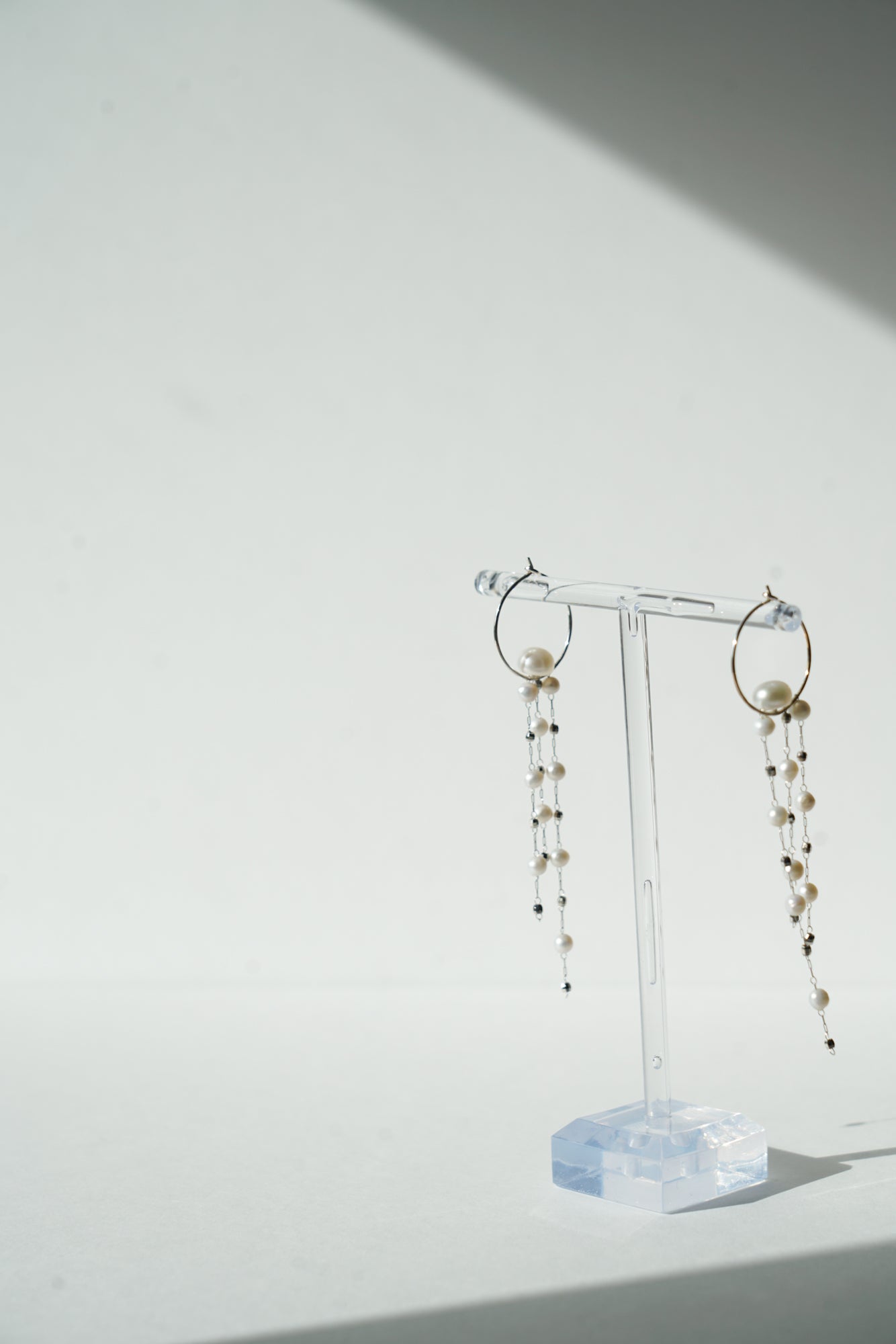 boucles d'oreilles pour mariée en mouvement sur un portant à bijoux transparent fait des des chaines perles naturelles