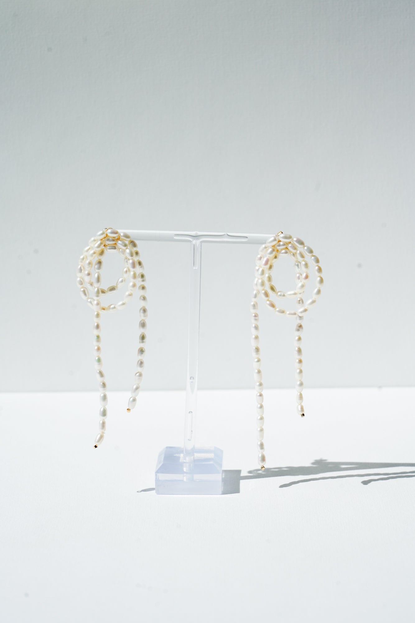 boucles d'oreilles moderne en perles naturelle pour un mariage posé sur un portant transparent