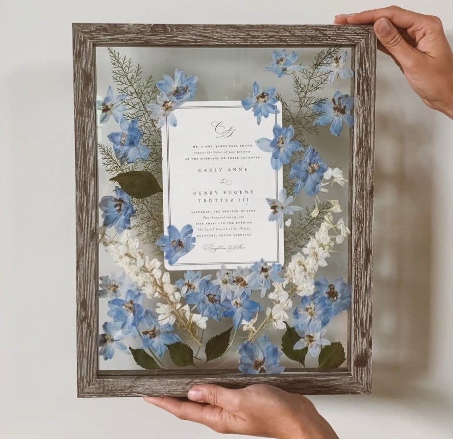 cadre décoratif avec des fleurs séchées bleues venant d'un bouquet de mariée et un papier avec un mot écrit dessus
