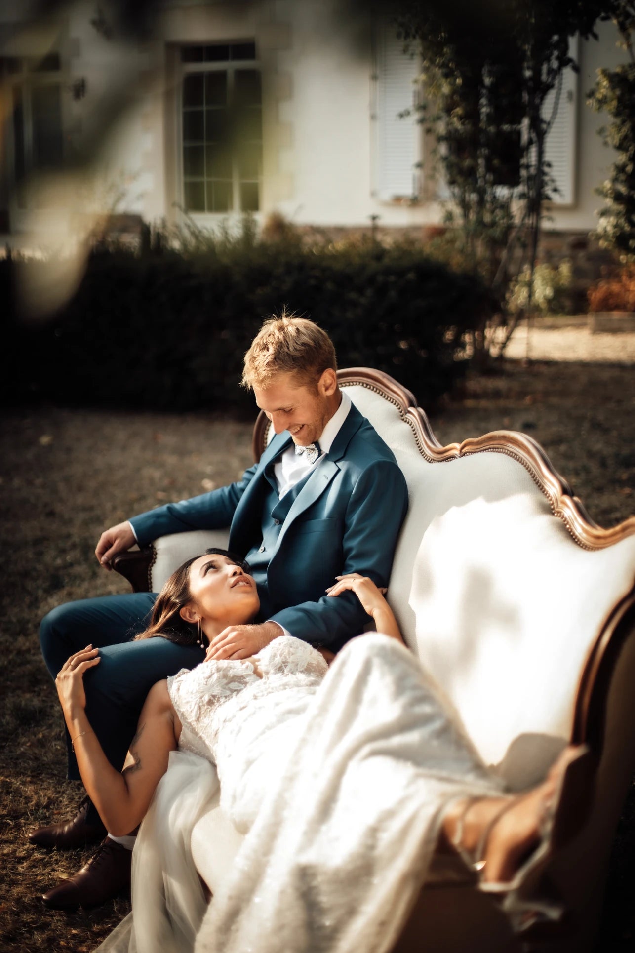 La mariée avec la tête sur les genoux du marié et qui se regardent dans leur tenue de mariage