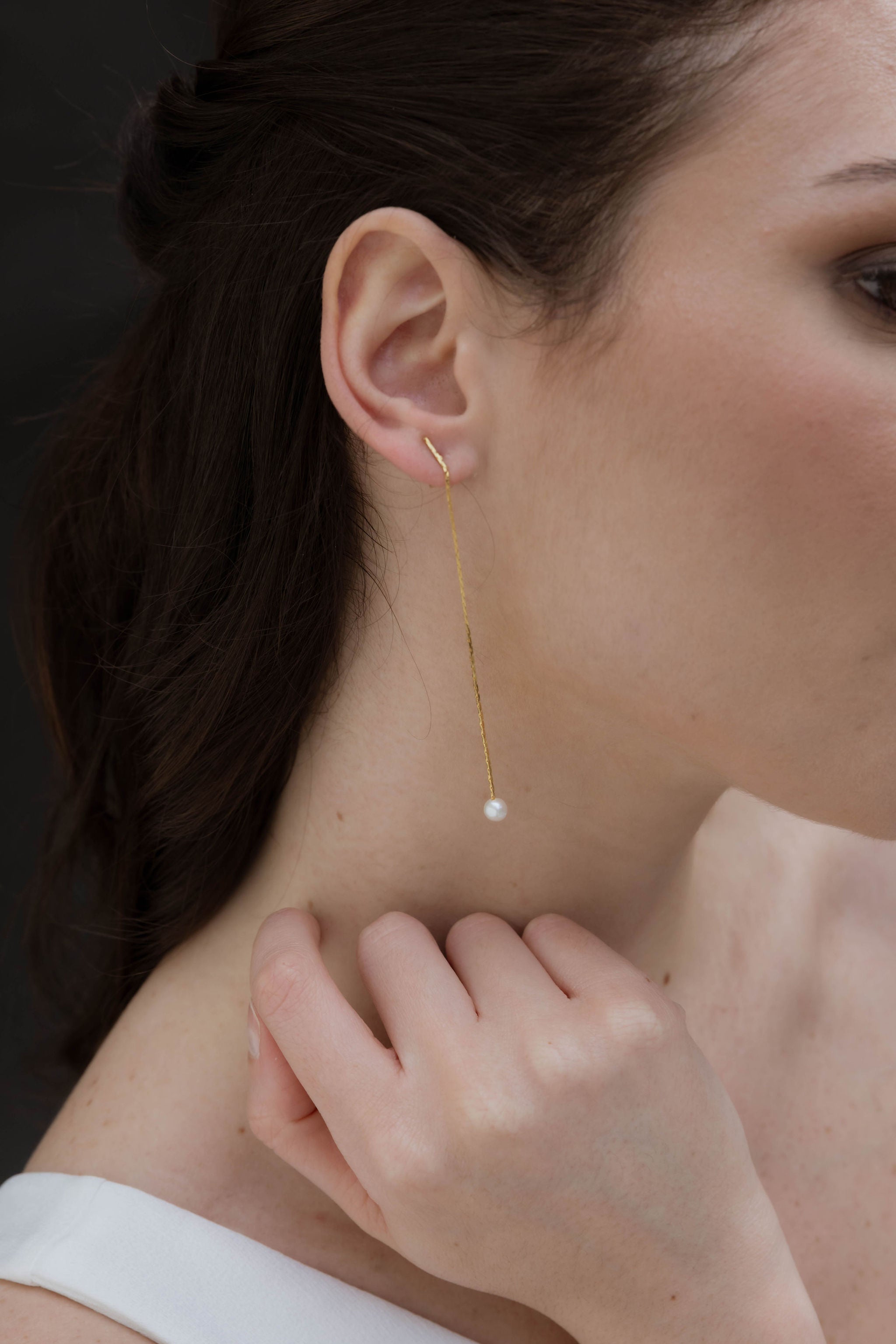 Focus sur les oreilles d'une femme portant des boucles d'oreilles pendantes de mariage minimaliste avec une perle naturelle