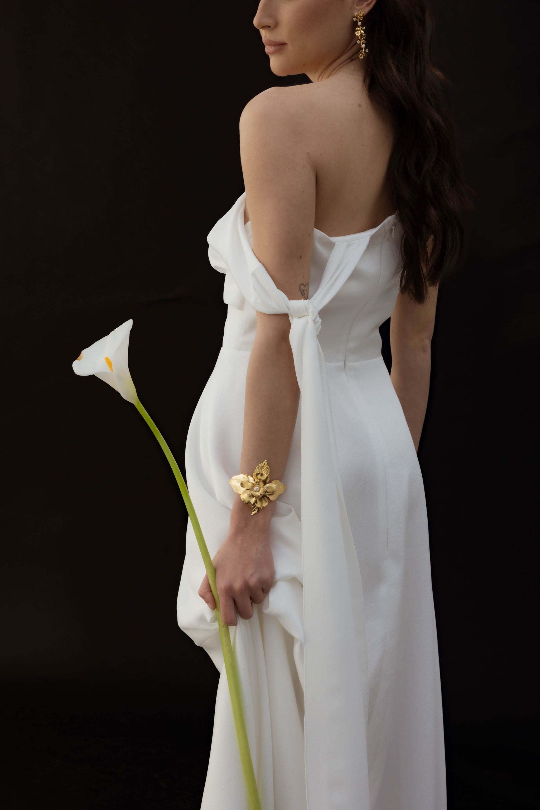 Femme de dos portant une fleur montrant ses accessoires de mariage comme ces boucles d'oreilles longues florales