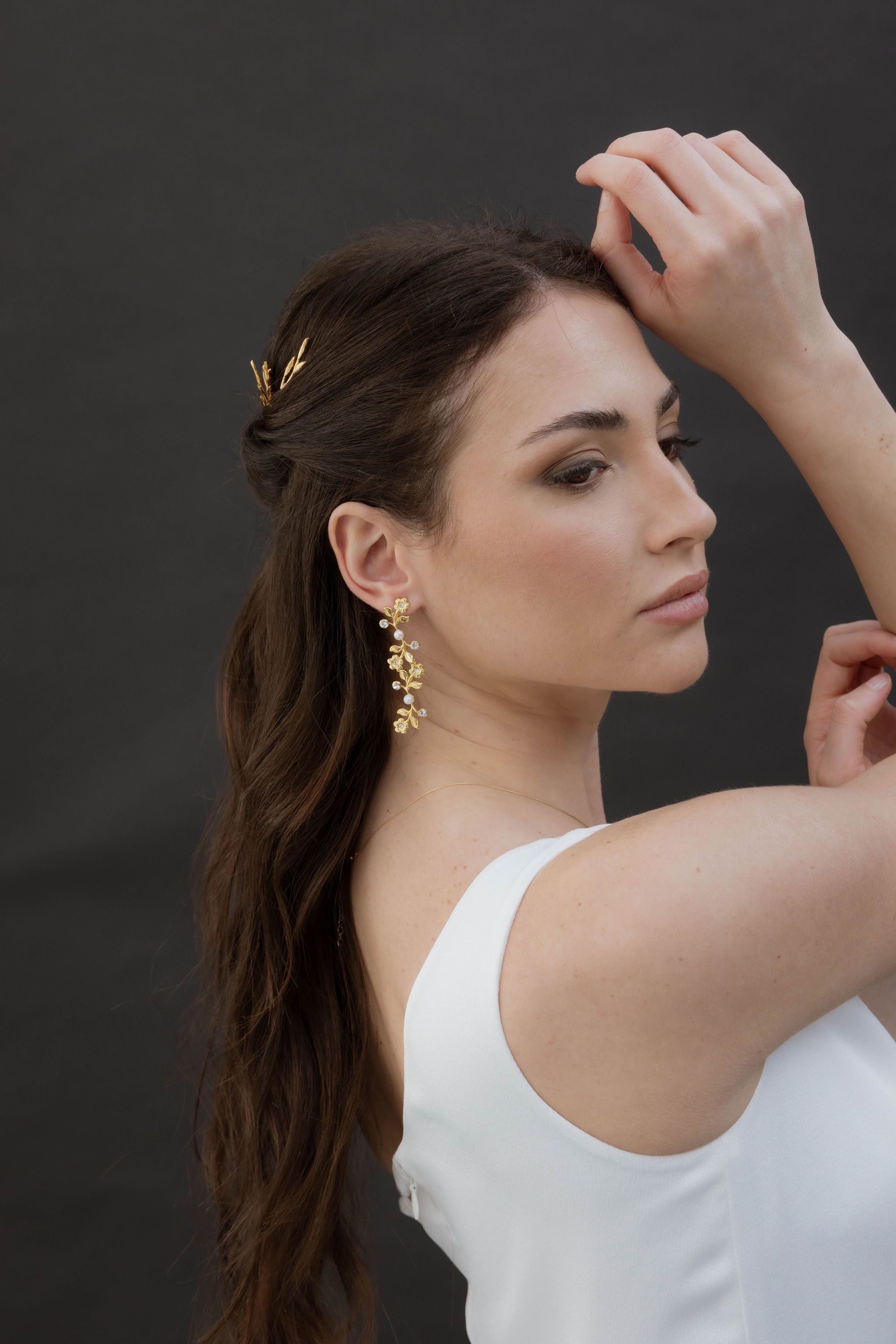 Femme avec le bras soutenant son visage de profil montrant ses boucles d'oreilles longues en fleurs avec perles et zircons