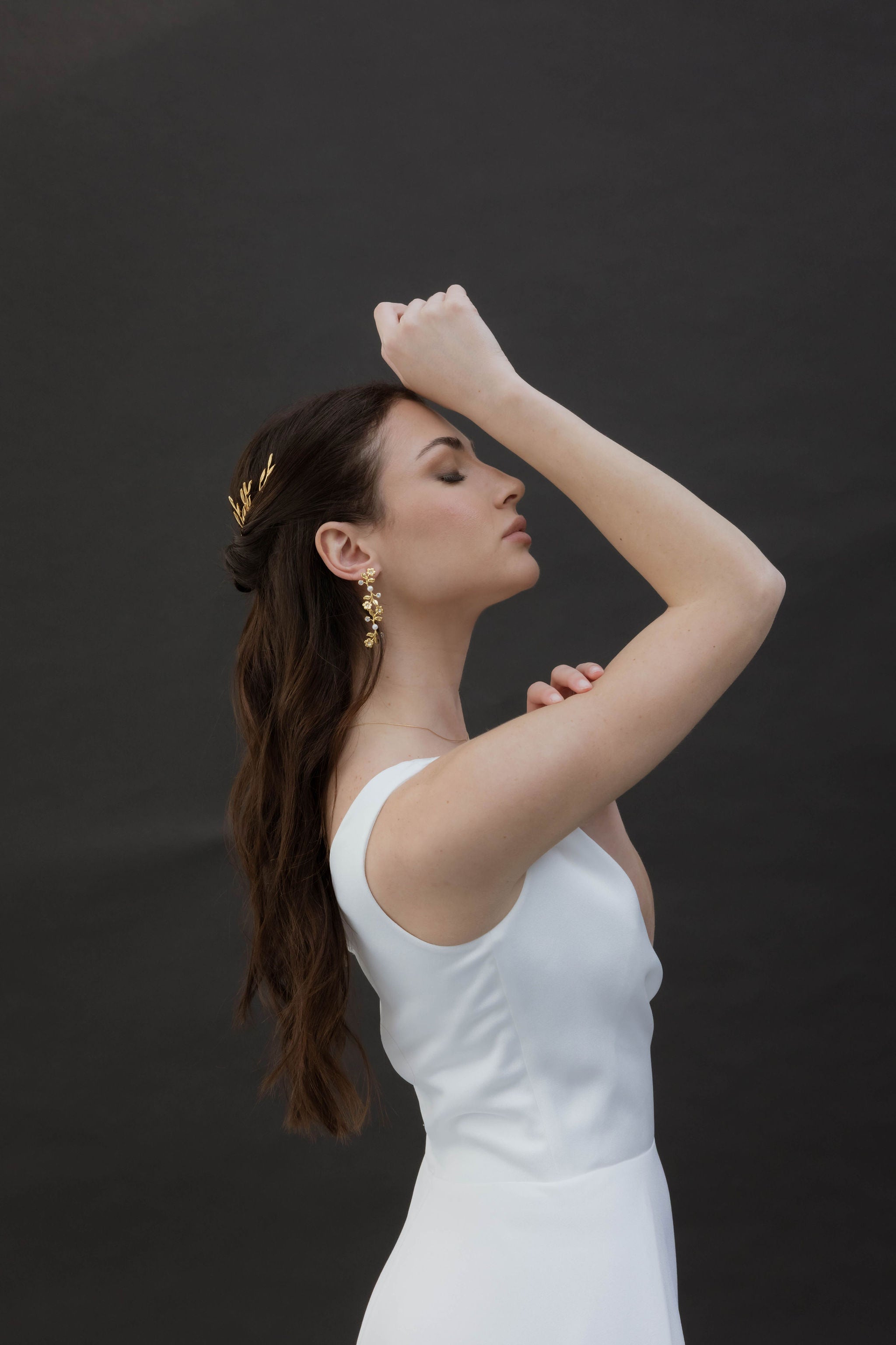 Femme de profil qui ferment les yeux, on aperçoit ses accessoires de mariage notamment ses boucles d'oreilles pour mariées romantique en perles naturelles et zircons