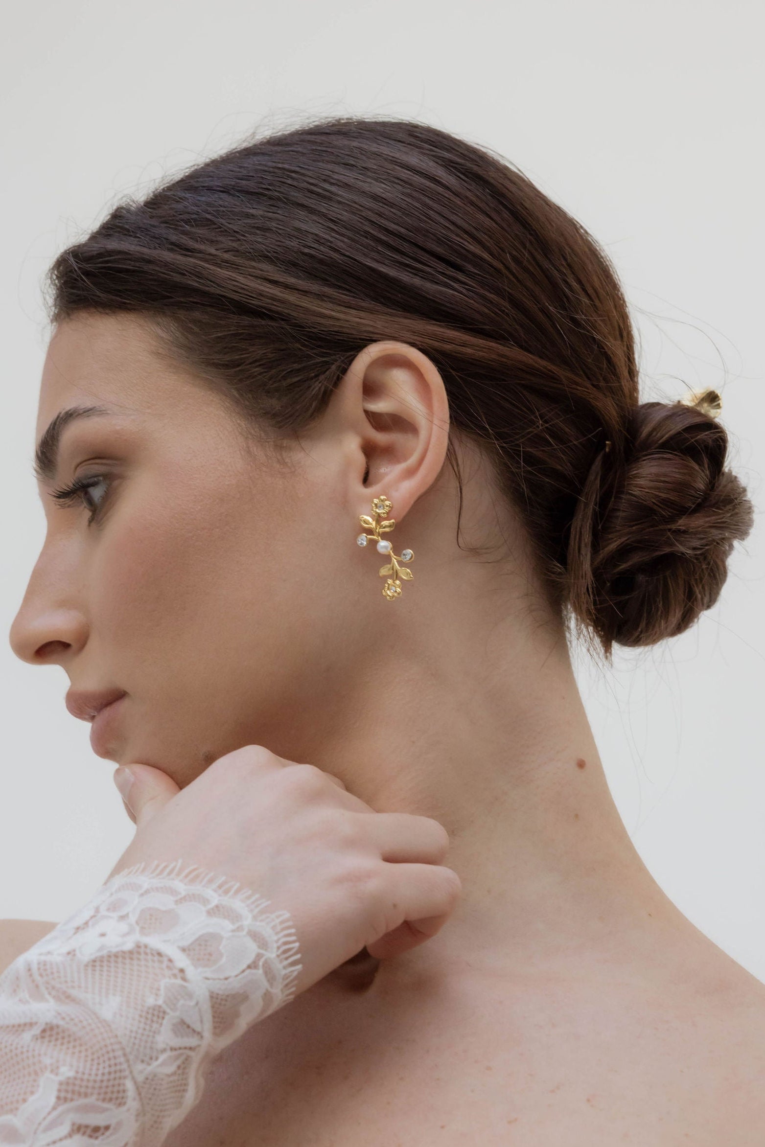Mariée de profil se touchant le menton, on peut voir sa boucle d'oreille mi-longue formant des fleurs avec des perles naturelles