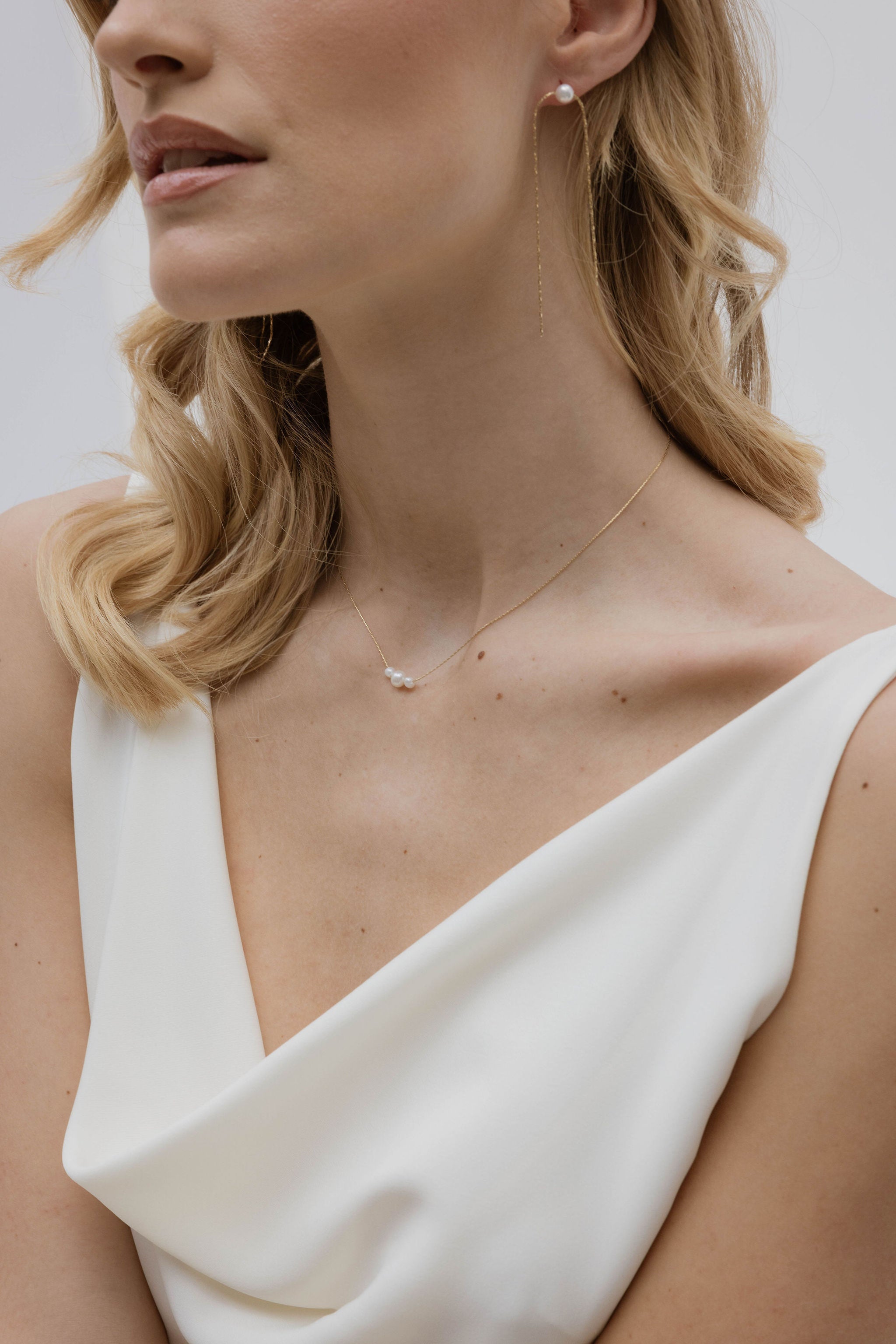 Focus sur le buste de la femme mettant en avant le son décolleté et son bijou de mariage collier et ses boucles d'oreilles fin en perles naturelles sur le devant