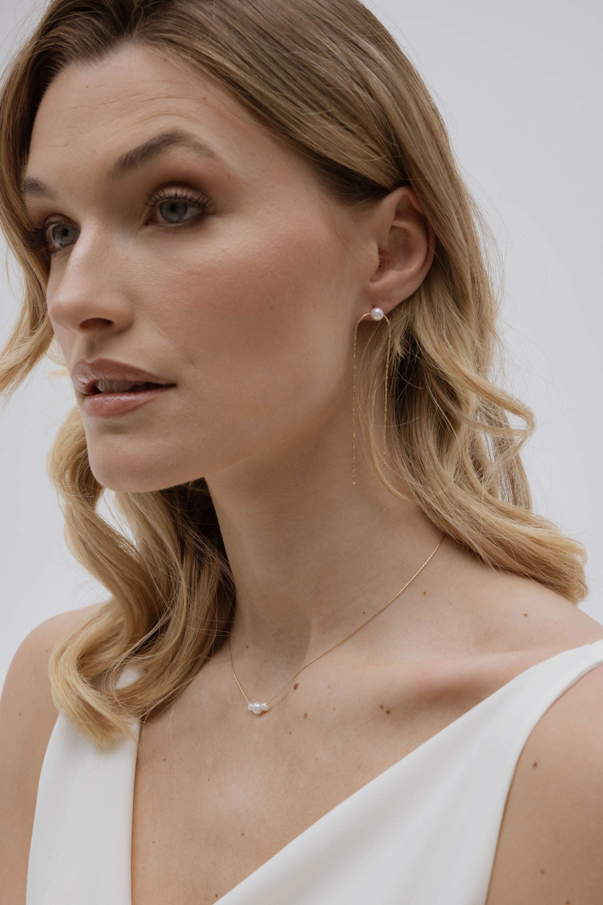 Femme de profil montrant sa parure de bijoux de mariée avec un collier en perle et des boucles d'oreilles minimalistes