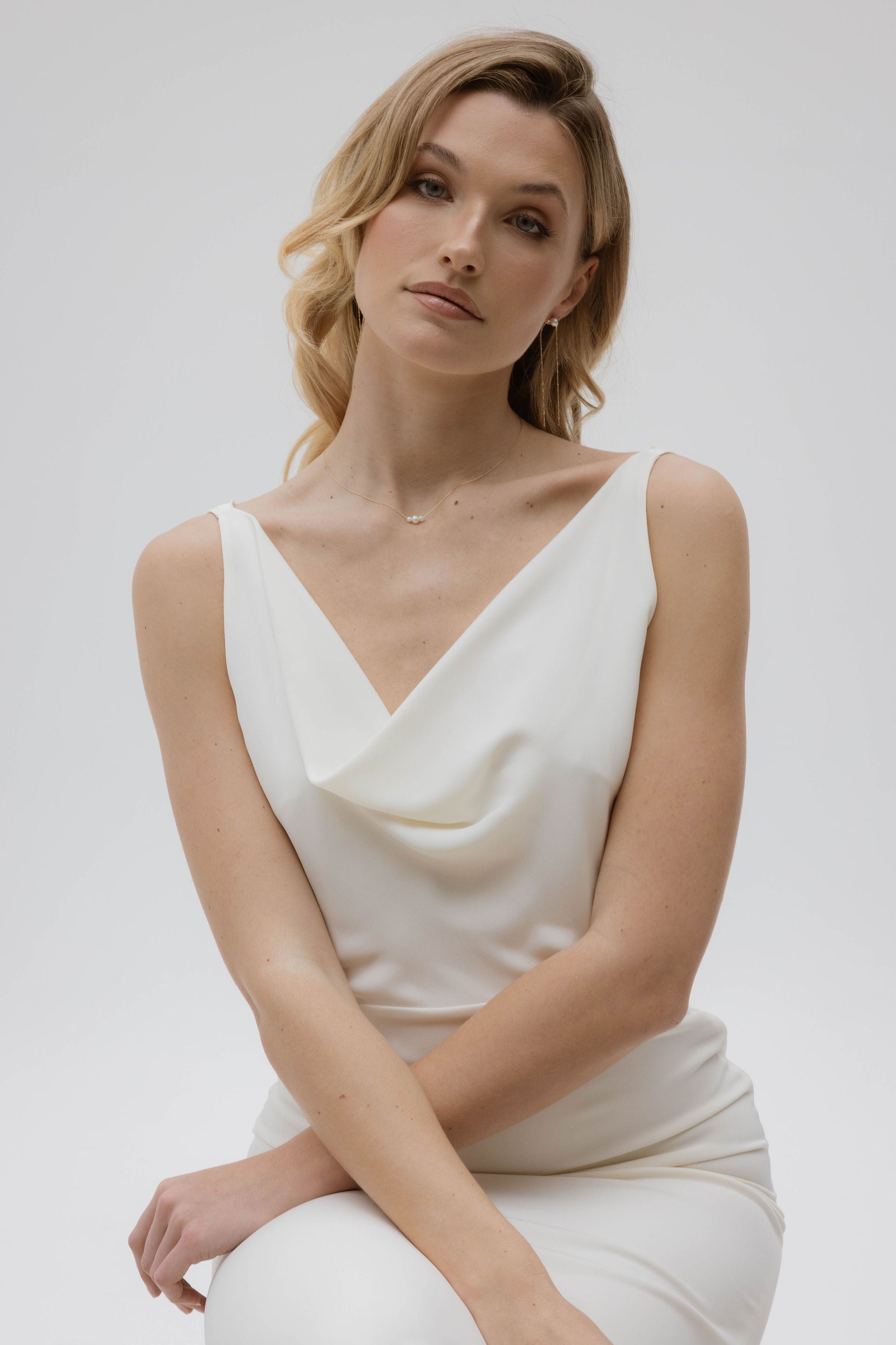 Mariée assise regardant l'objectif les bras croisé mettant en évidence ses accessoires de mariage en perle naturelle