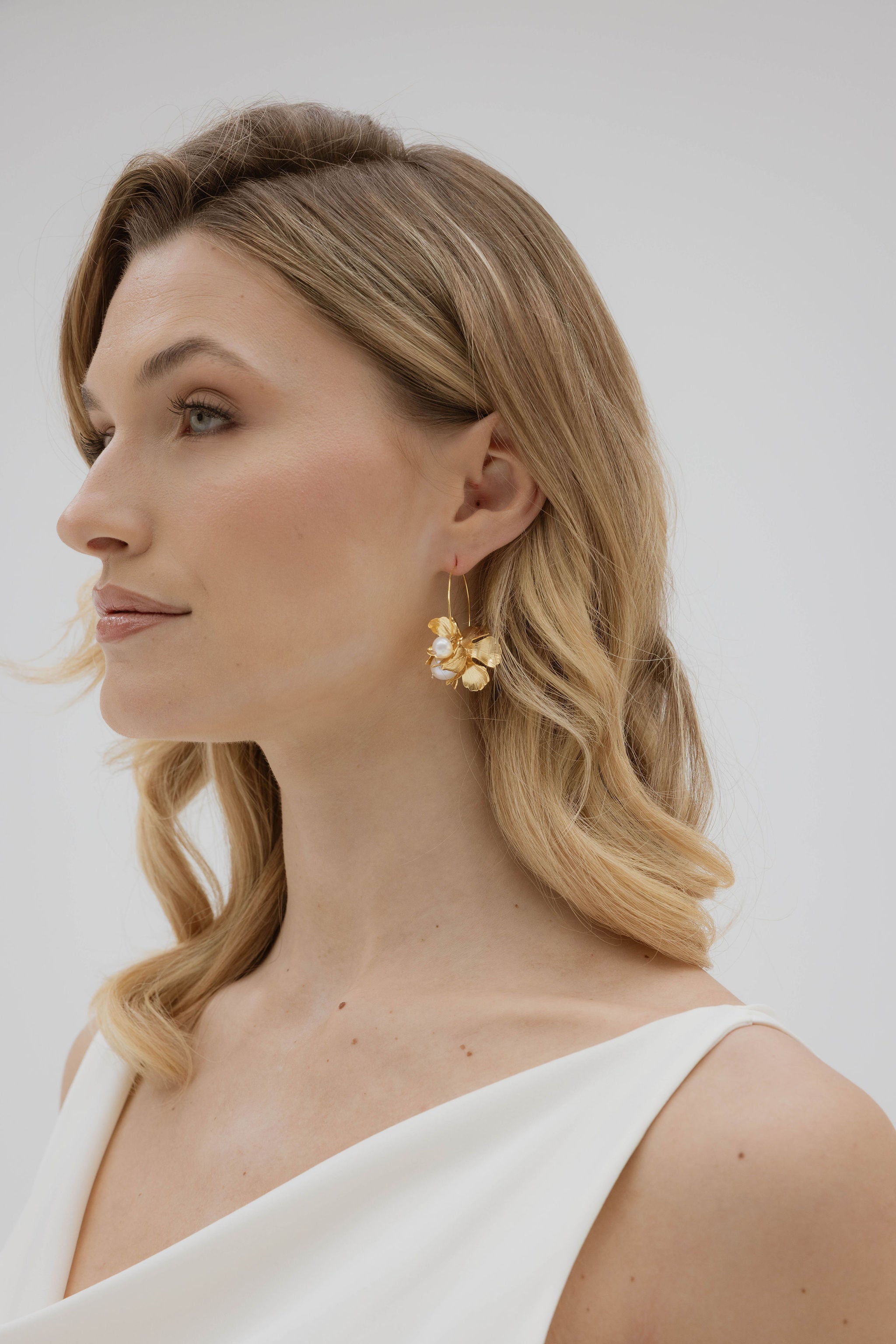 Femme de profil montrant ses créoles de mariage avec une finition en fleur avec des perles de cultures