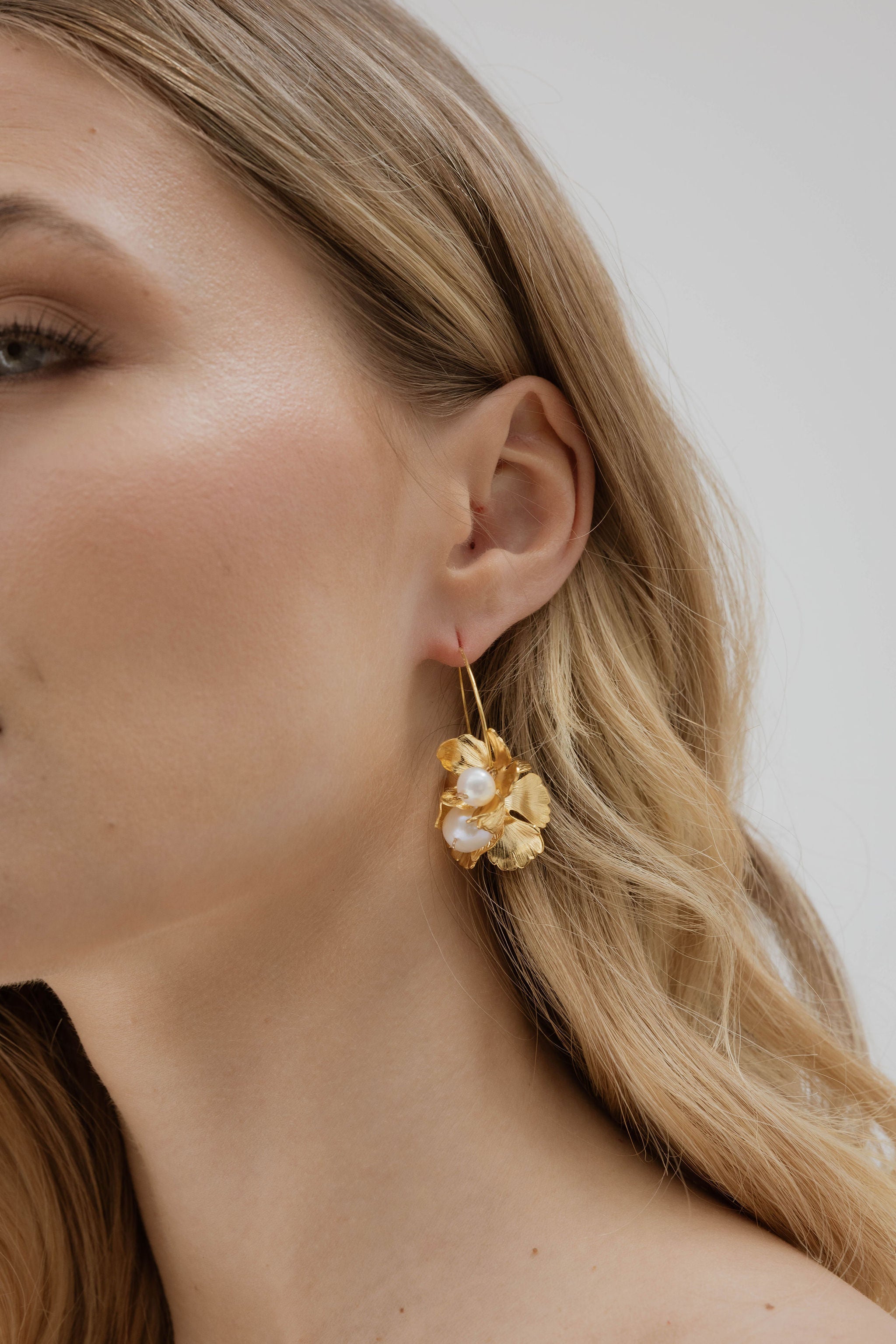 Focus sur l'oreille d'une mariée portant une boucle d'oreilles pendantes avec une finition printanière avec des feuilles