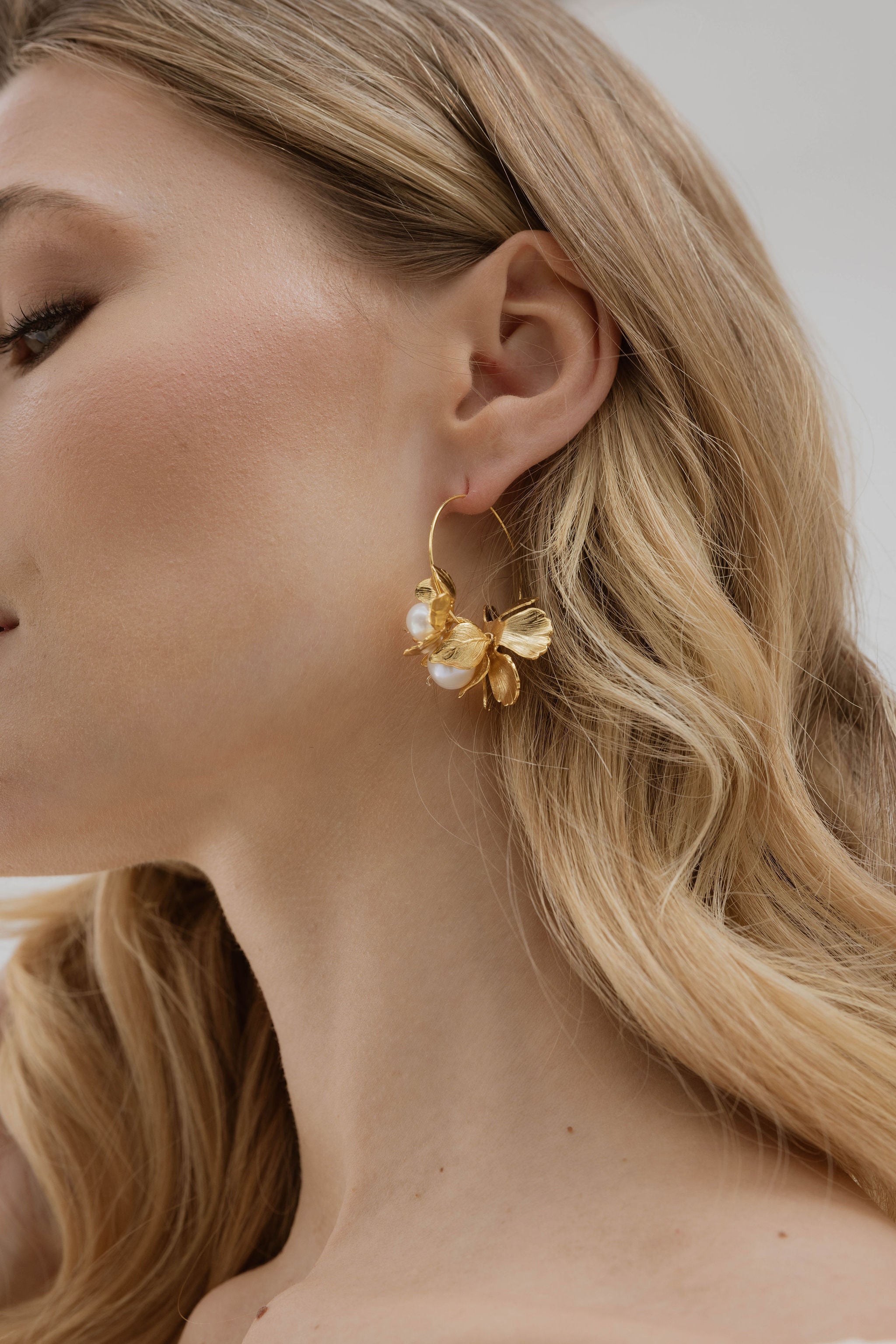 Focus sur l'oreille d'une mariée portant des boucles d'oreilles en cercle avec fleurs et perles naturelles