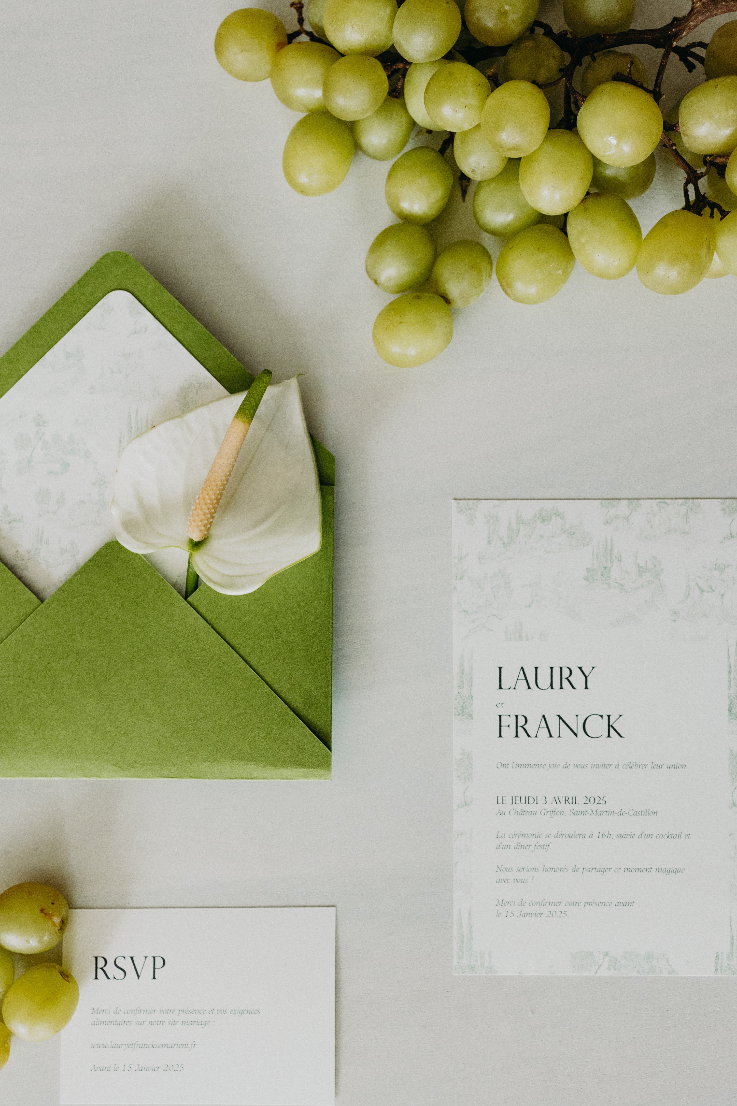 Papèterie sur le thème matcha et olive, enveloppe couleur matcha accompagnée d'élégants et modernes RSVP et faire parts ainsi que d'une fleur et de raisins.