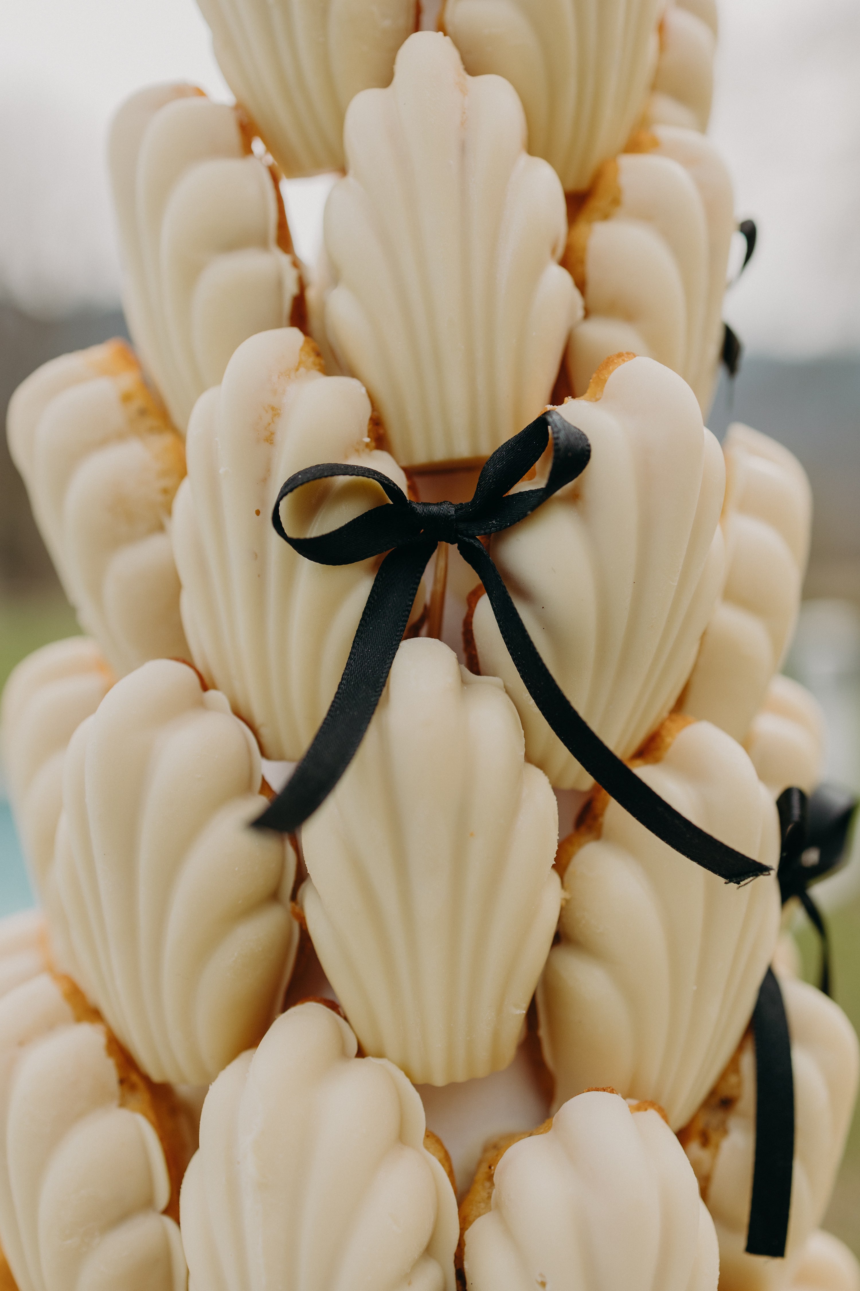 Pièce montée originale composée de madeleines, joliment ornée de petits rubans noirs, dans une ambiance mariage moderne et naturel aux tons matcha et olive, pour une inspiration gourmande et élégante