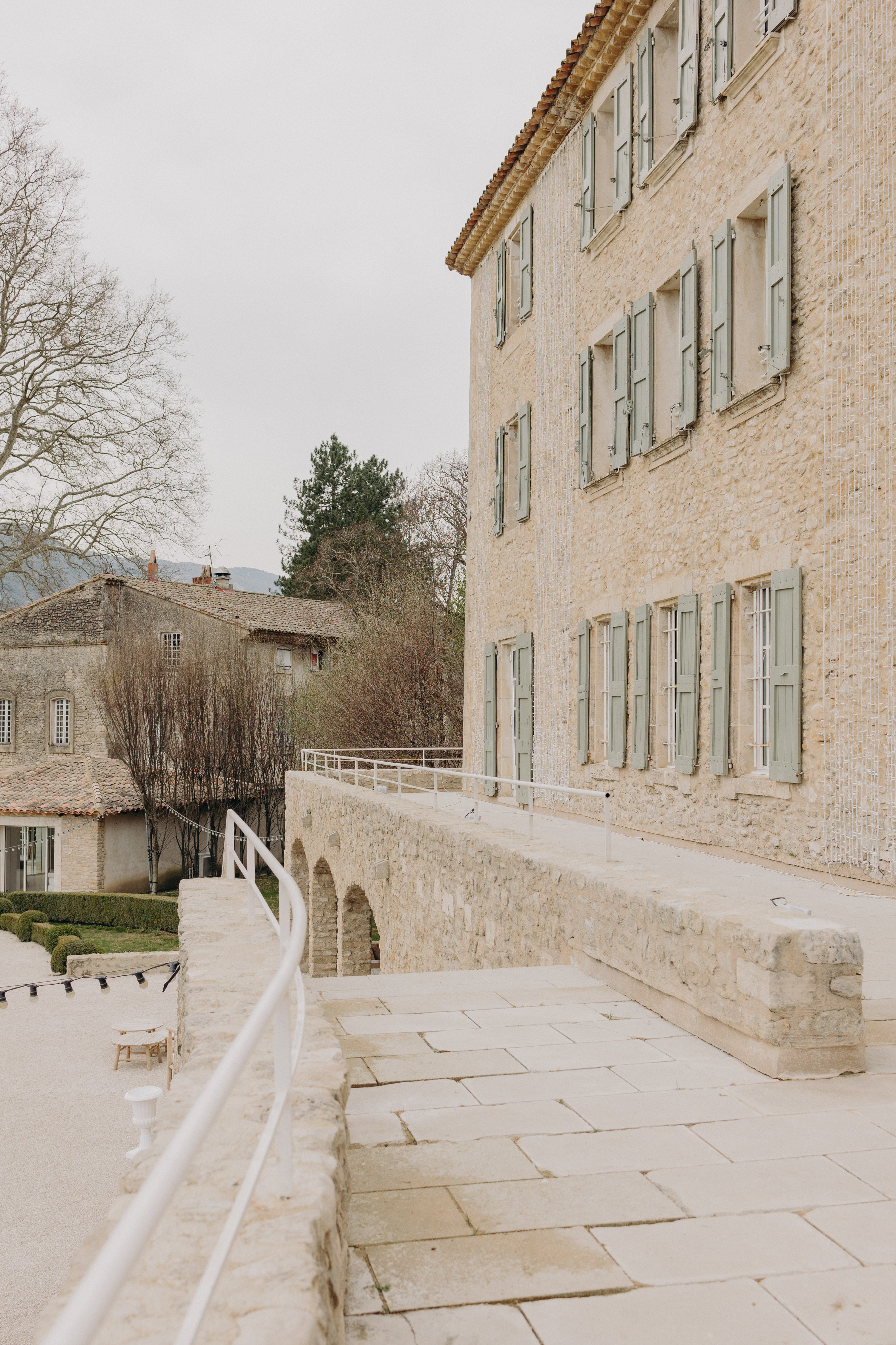 Décor de chateau très élégant et épuré pour un mariage naturel sur le thème matcha et olive, on voit une façade de chateau et des volets verts pastel, des arbres et un escalier en pierres.