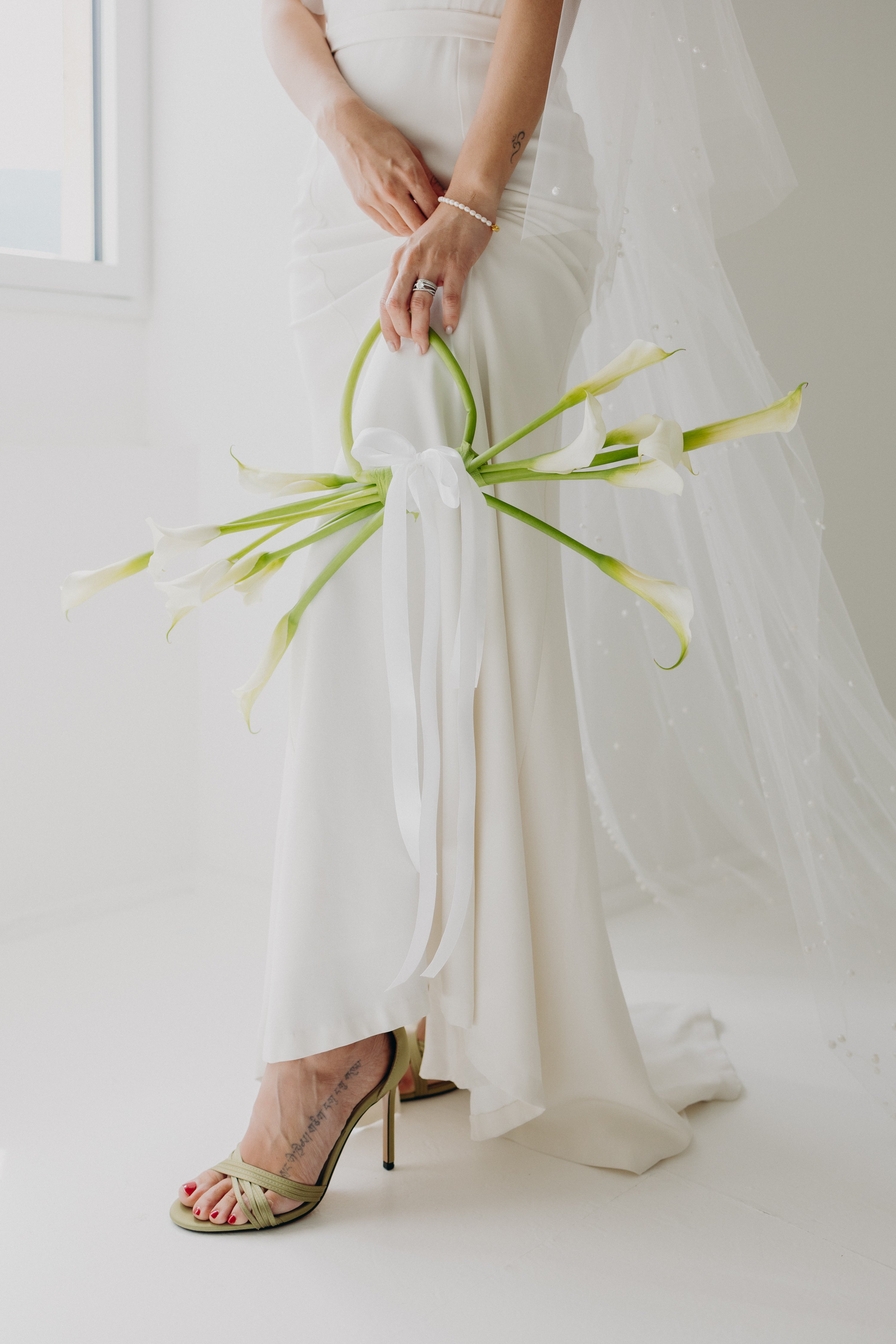 Bouquet de fleurs moderne et tendance, aux fleurs délicates et verdure naturelle, avec une tige transformée en anse façon sac, pour une inspiration mariage moderne et naturel aux tons matcha et olive.