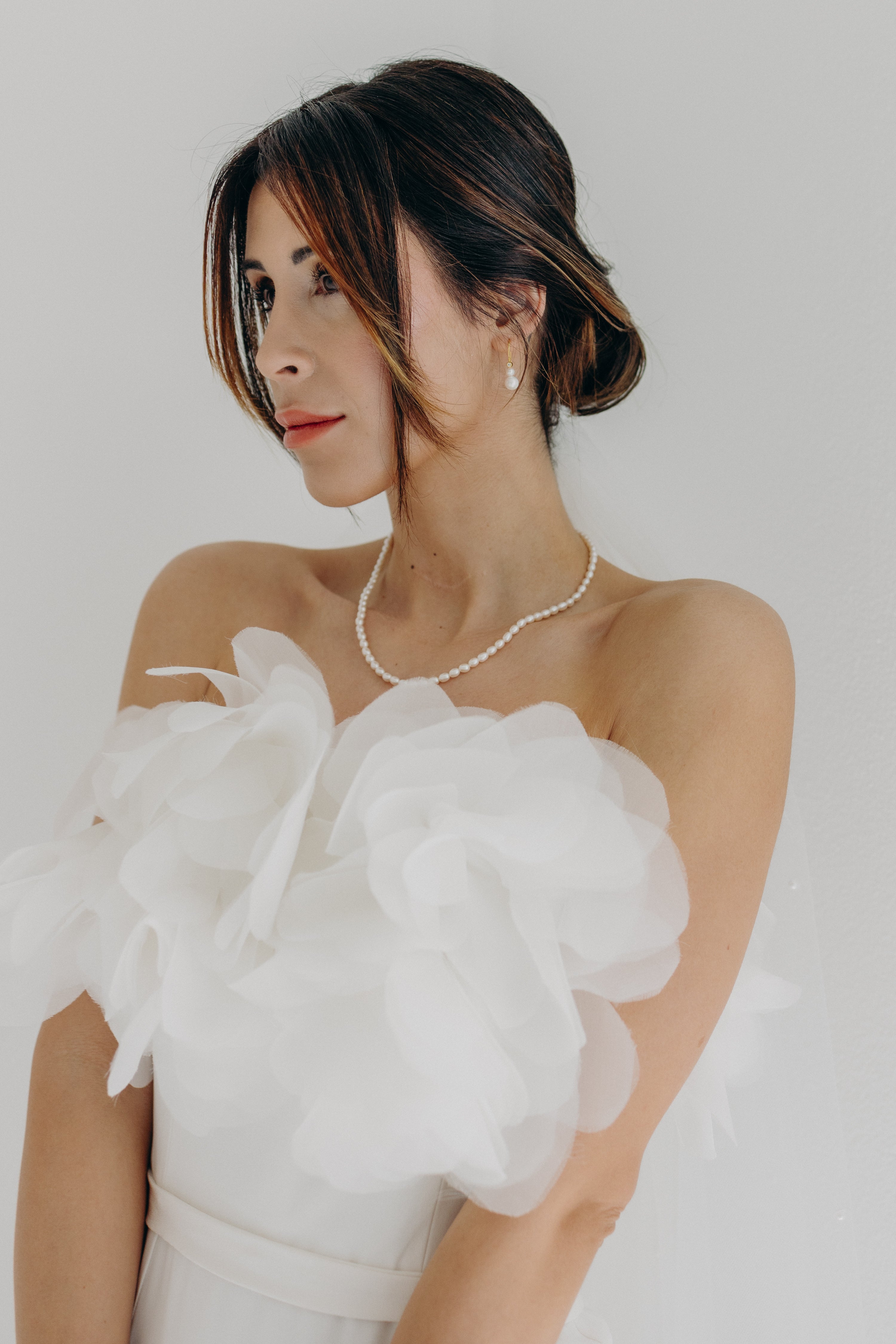 Mariée élégante et raffinée portant de sublimes accessoires signés Atelier Lilac, un magnifique collier de perles et des boucles d'oreilles assorties avec un joli chignon bas naturel et moderne pour un mariage inspiration matcha et olive, moderne et naturel .