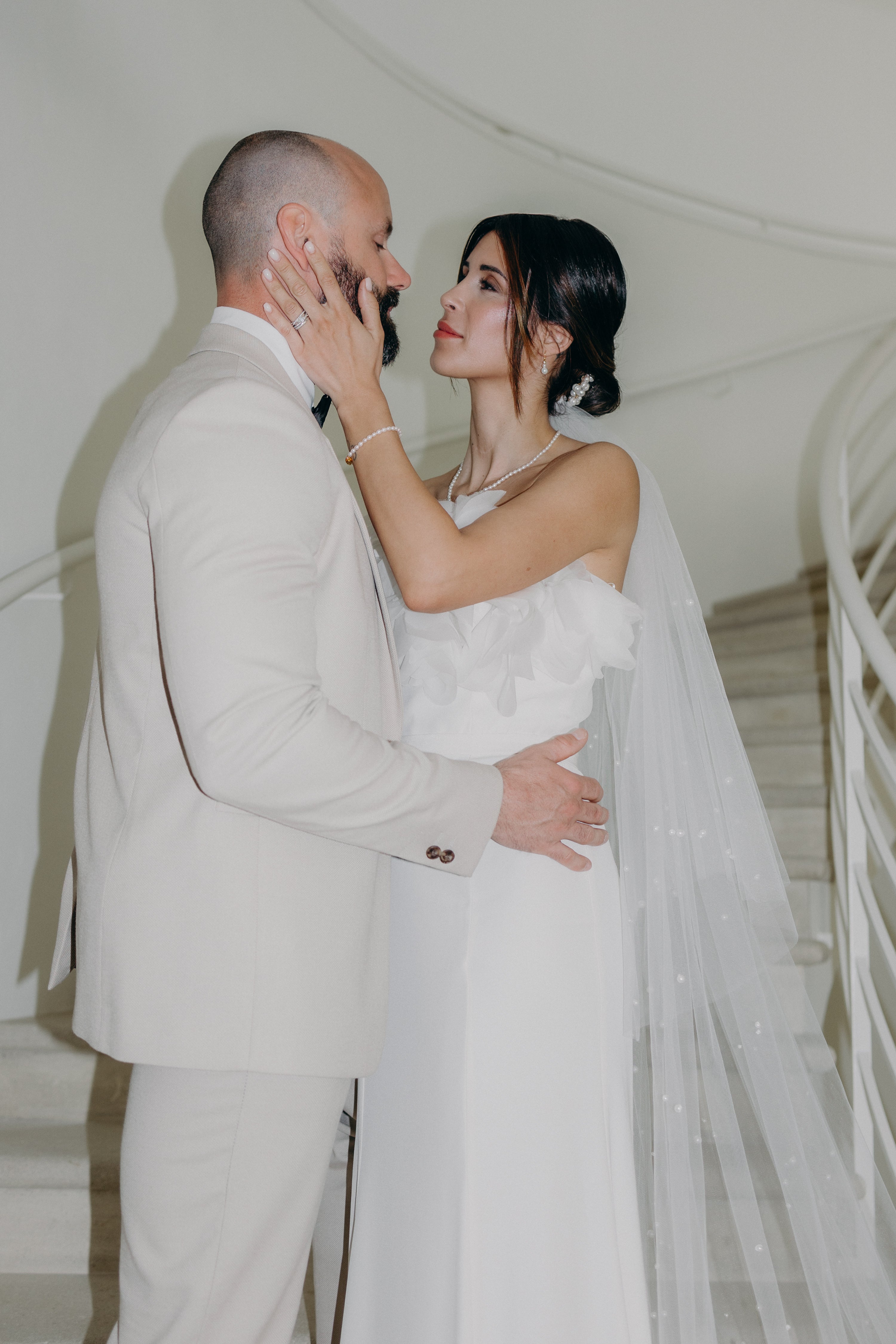 Les mariés enlacés devant l’escalier d’un château, dans une ambiance naturelle et raffinée aux tons matcha et olive, avec la mariée sublimée par des bijoux Atelier Lilac, artisanaux et poétiques.