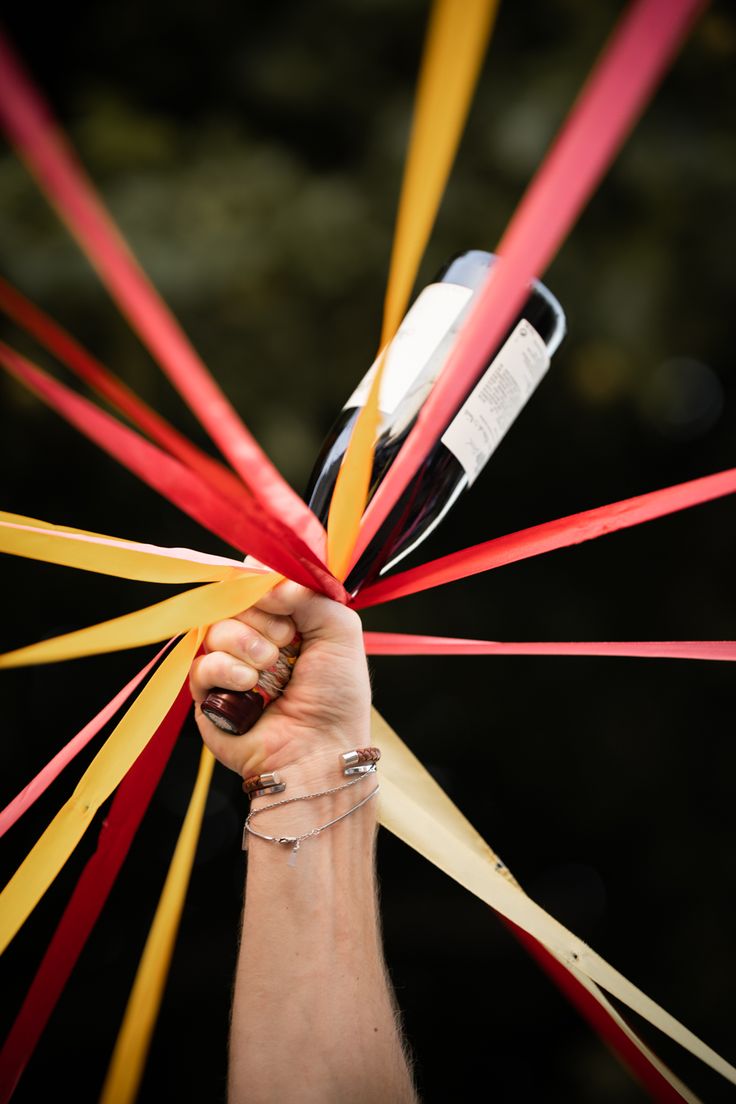main d'un homme tenant en hauteur une bouteille de vin dans la main avec des rubans accrochés