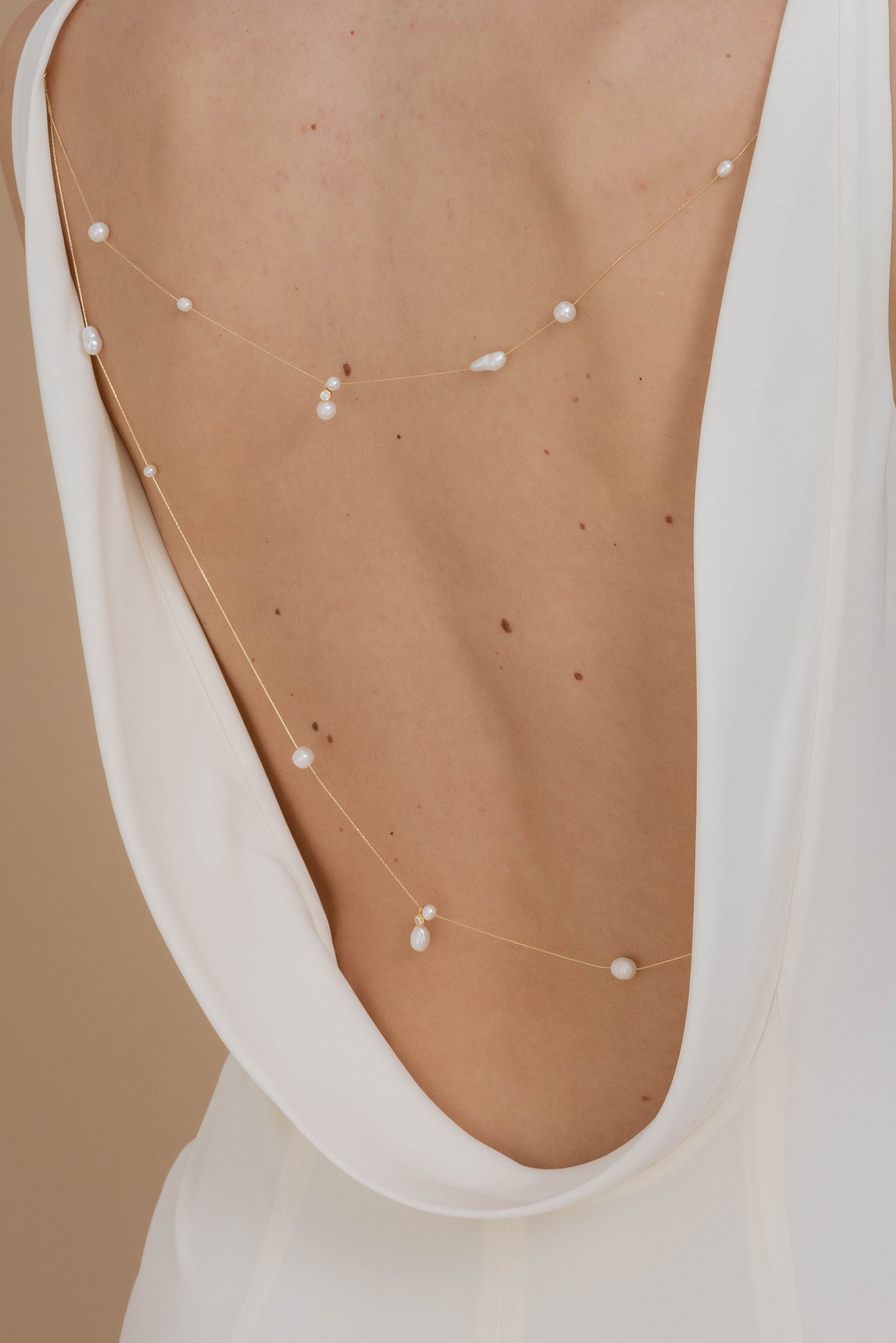 Focus sur le decolleté de dos d'une mariée montrant son bijou de dos fait de perles naturelles baroque