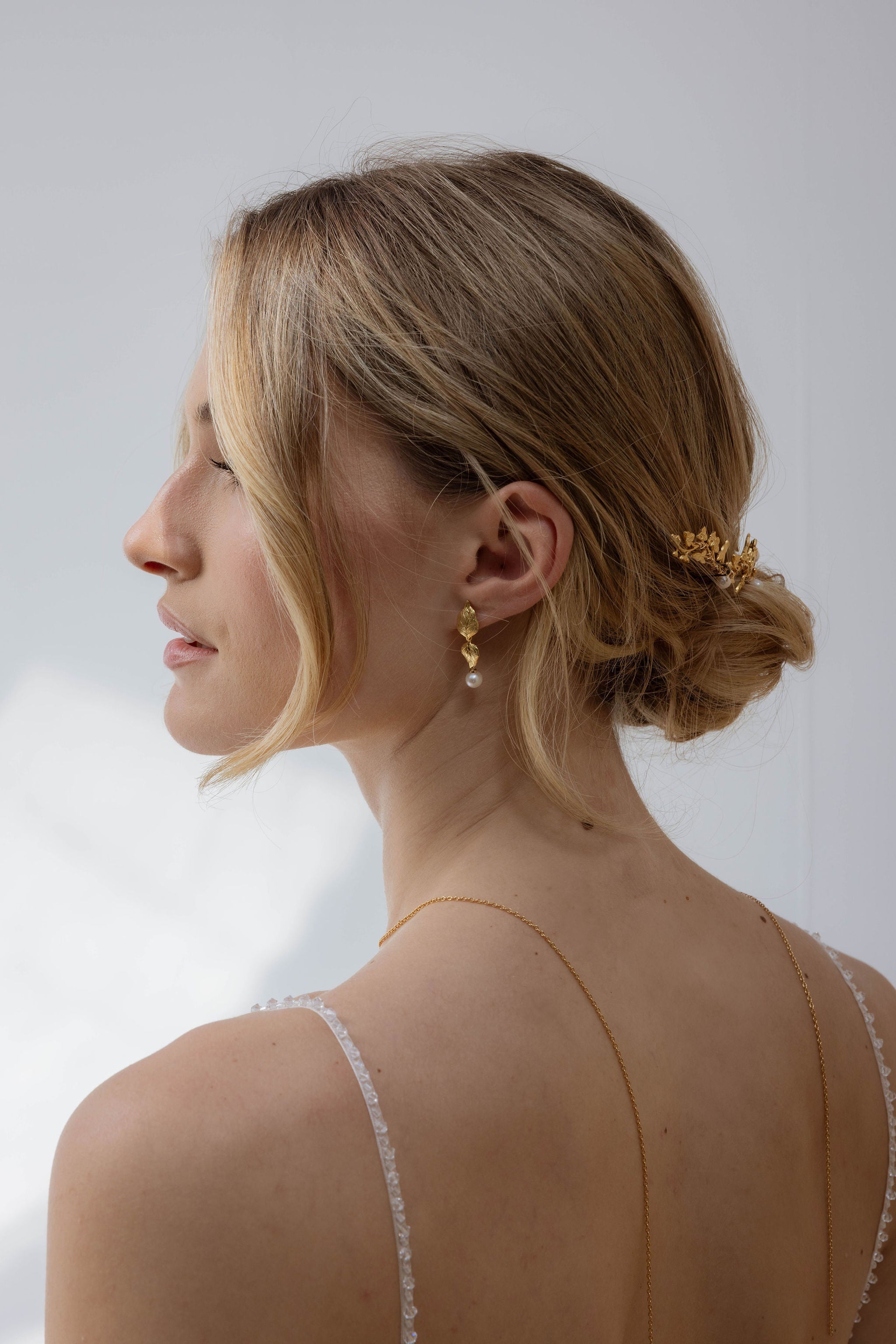 Femme de profil mettant en avant sa parure de bijoux pour mariée florale et matériaux type perles