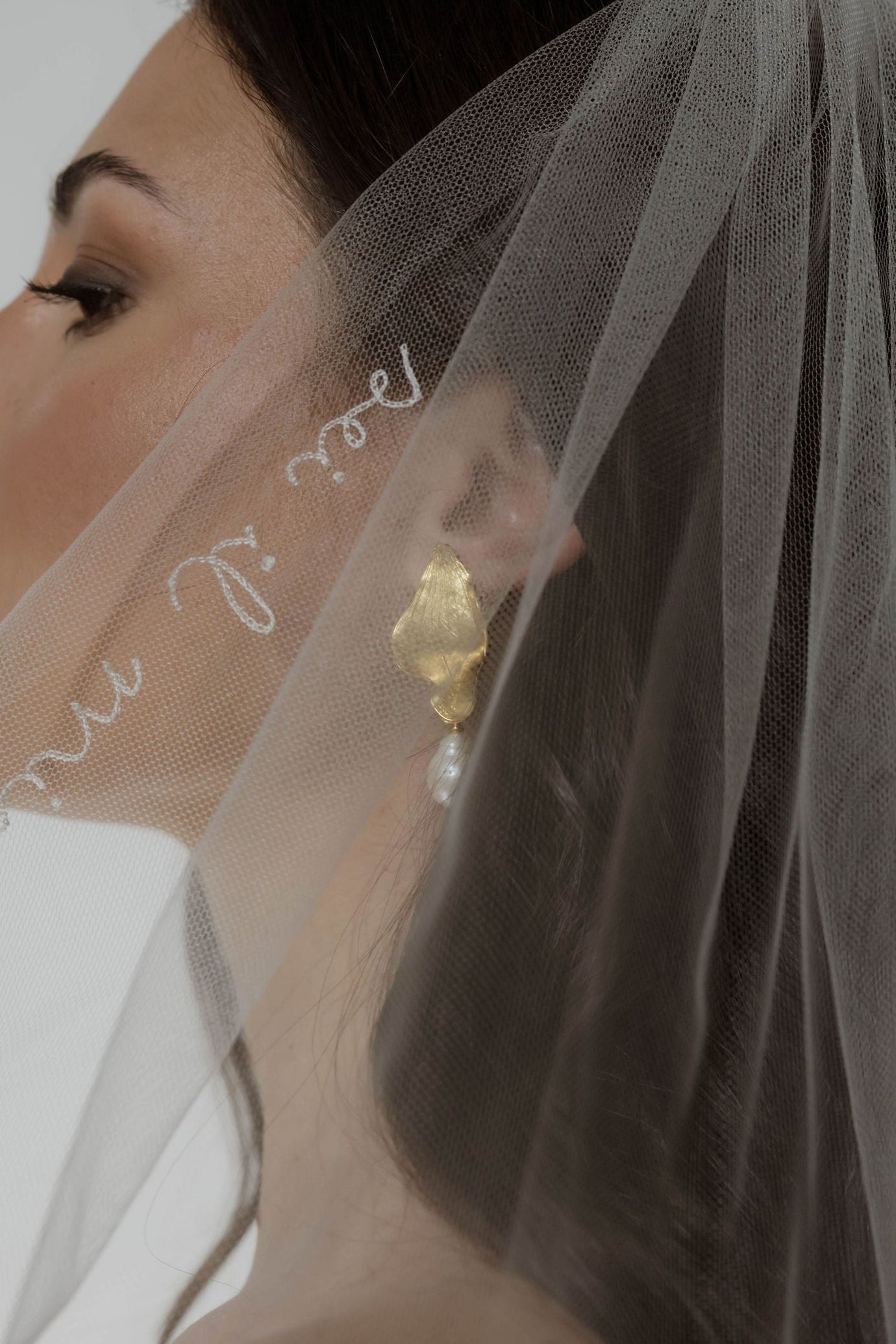 Mariée de profil portant un voile devant ses boucles d'oreilles de fêtes en forme de fleurs avec une perle baroque