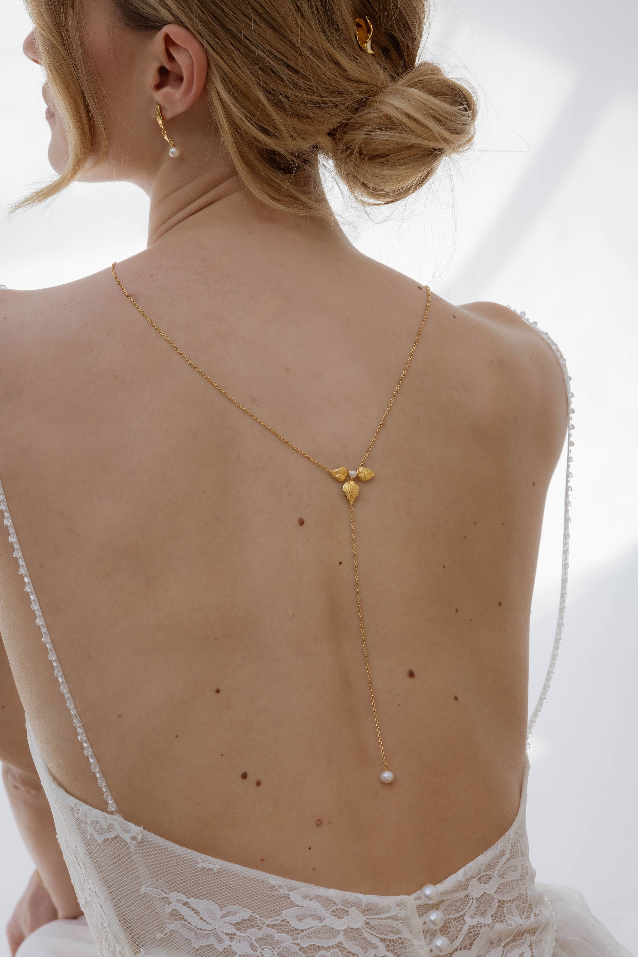 Femme de dos avec un collier de dos de mariage en forme de fleur avec une finition en perles naturelles