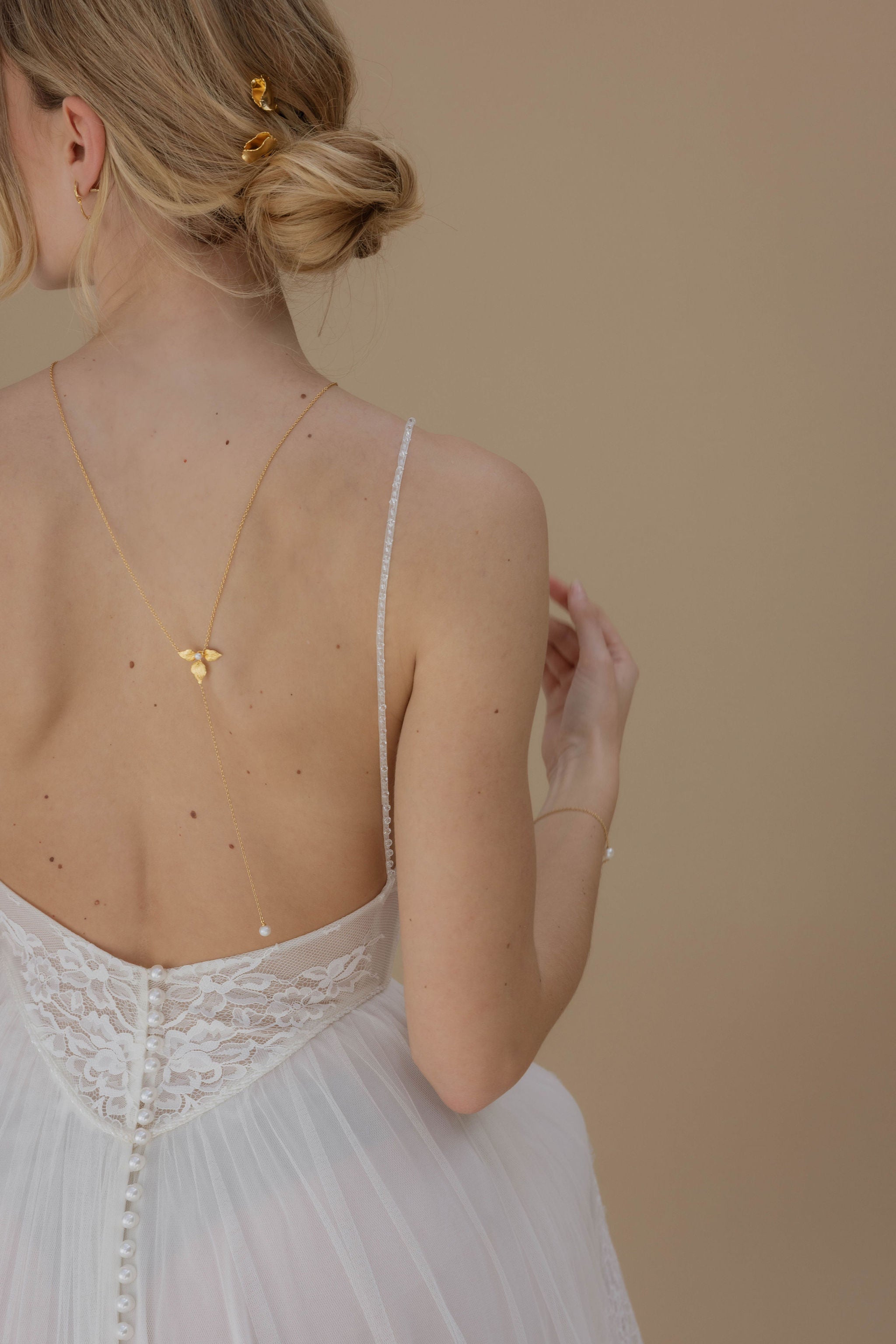 Femme de dos dans une robe de mariée mettant en avant son décolleté de dos et son bijou de dos fleuri avec sa coiffure de mariage orné de pics en fleurs