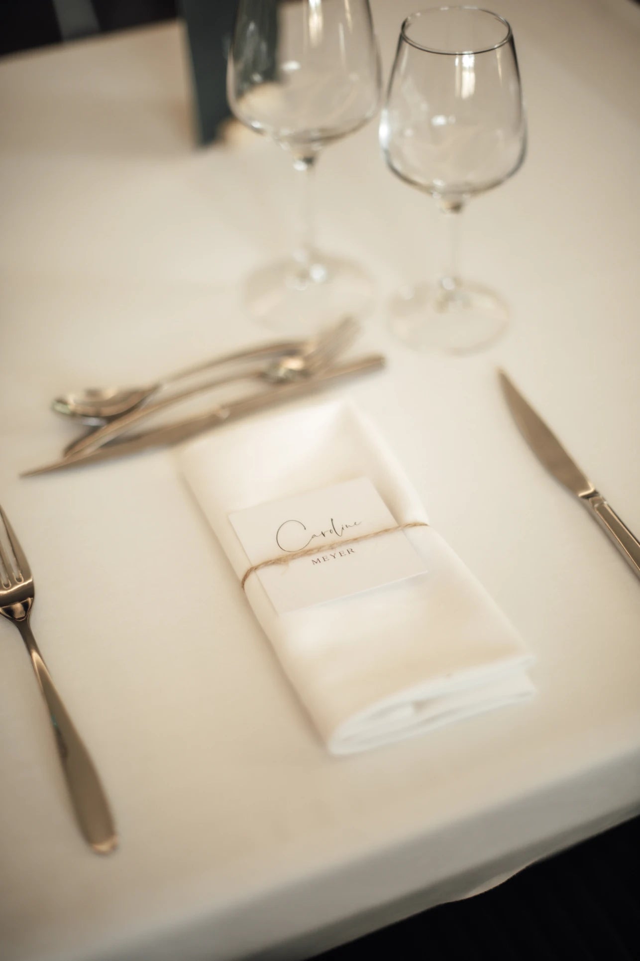Serviette plié entourée des couverts avec au dessus une carte avec le nom des invités