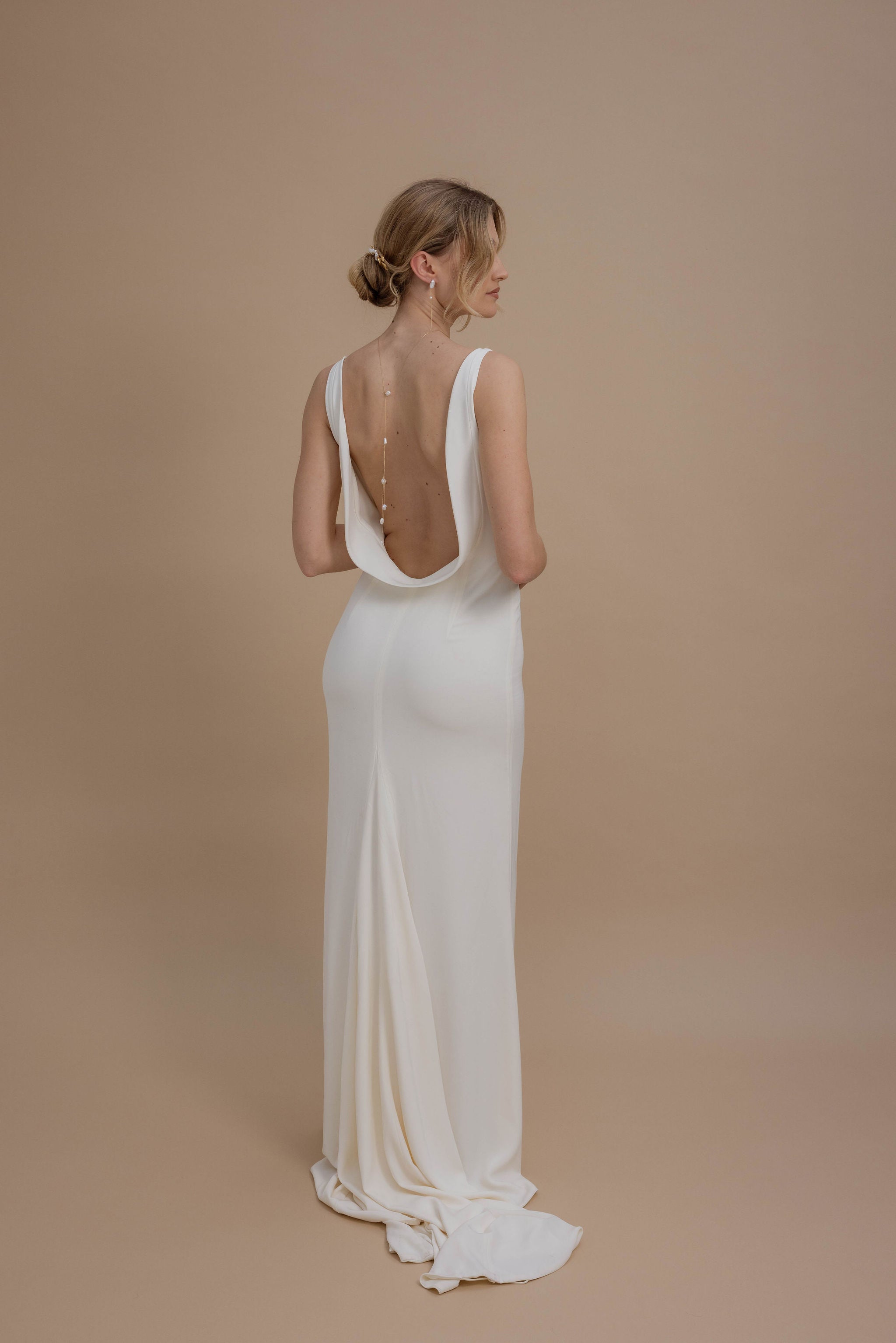 Femme dans sa robe de mariage montrant sa parure de bijoux de dos avec son collier de dos et ses boucles d'oreilles en perles baroque